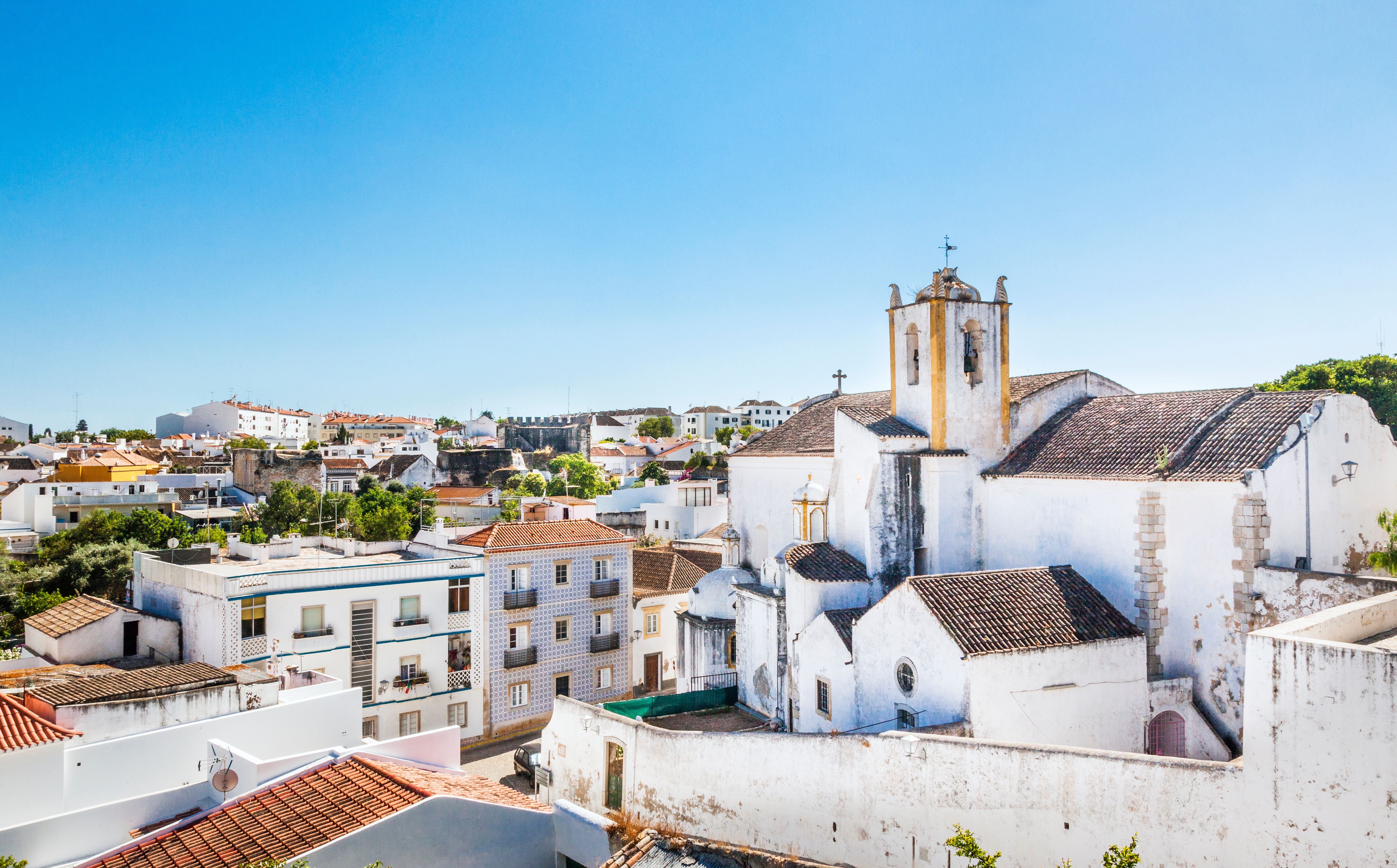 Blick auf die Kirche Santiago in Tavira, Algarve, mit weißen Häusern und blauem Himmel.