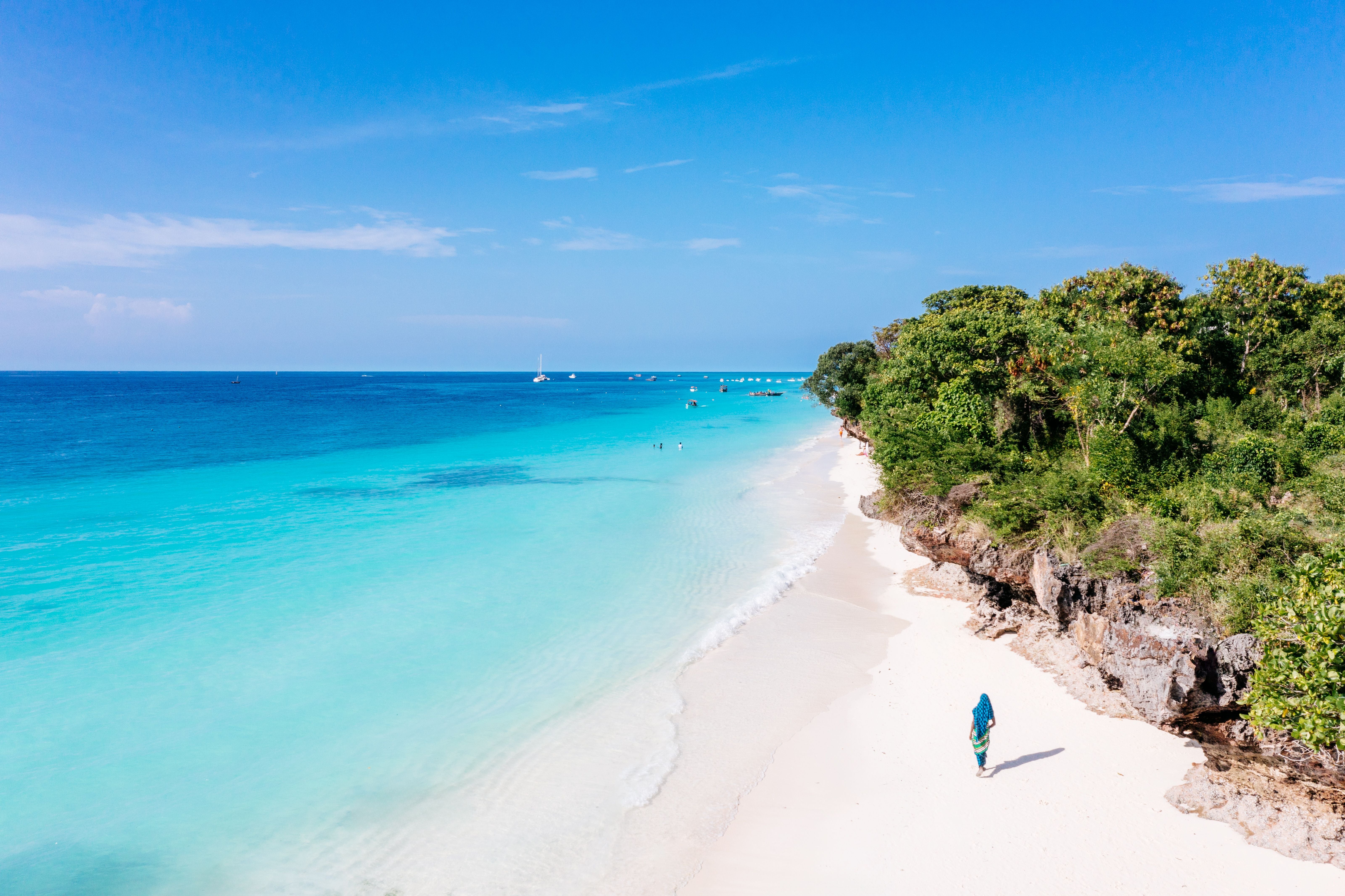 Frau läuft am weißen Sandstrand mit türkisblauem Wasser in Nungwi, Zanzibar entlang.