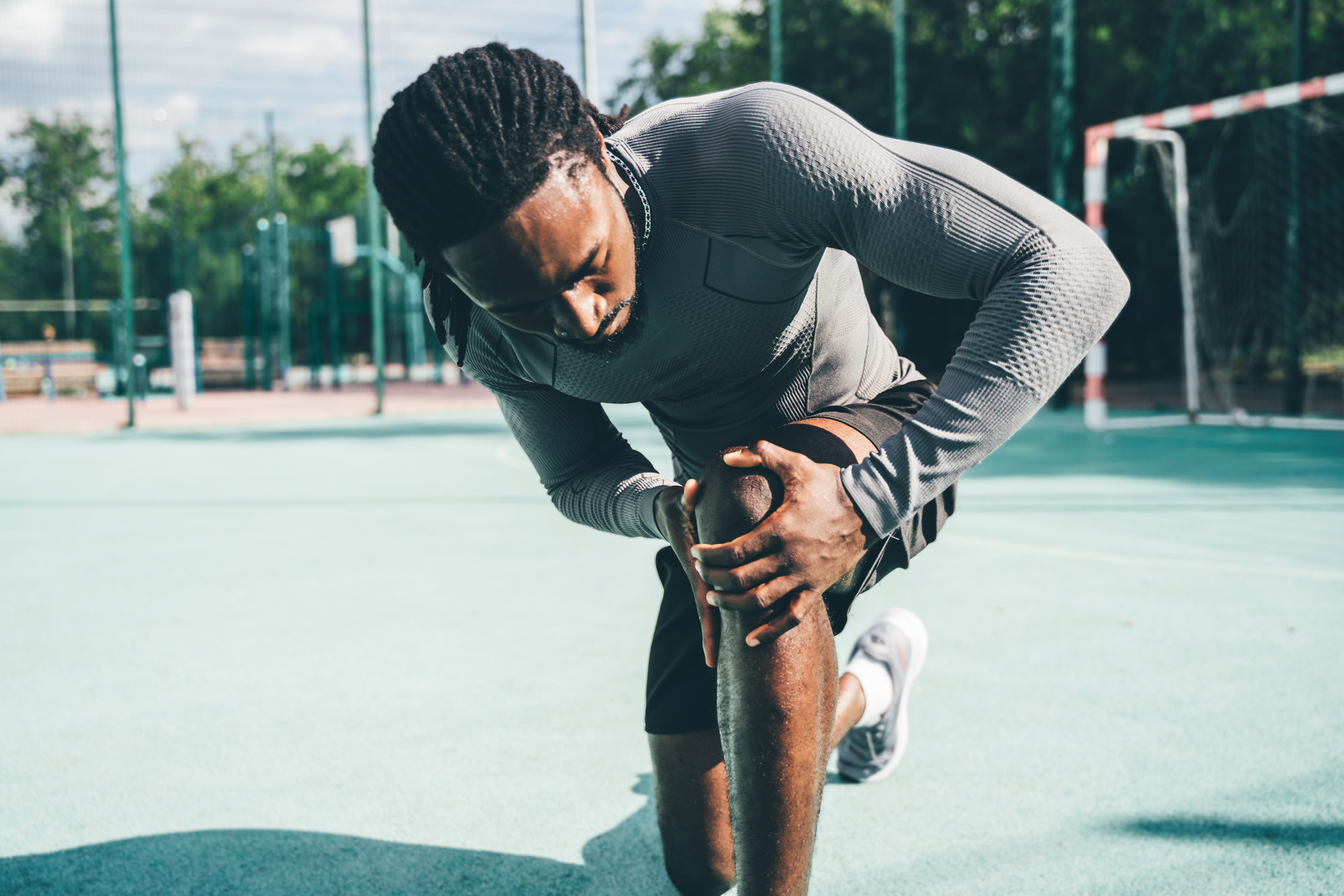 Mann im Sportoutfit dehnt sich und hält sein Knie auf einem Outdoor-Sportplatz.