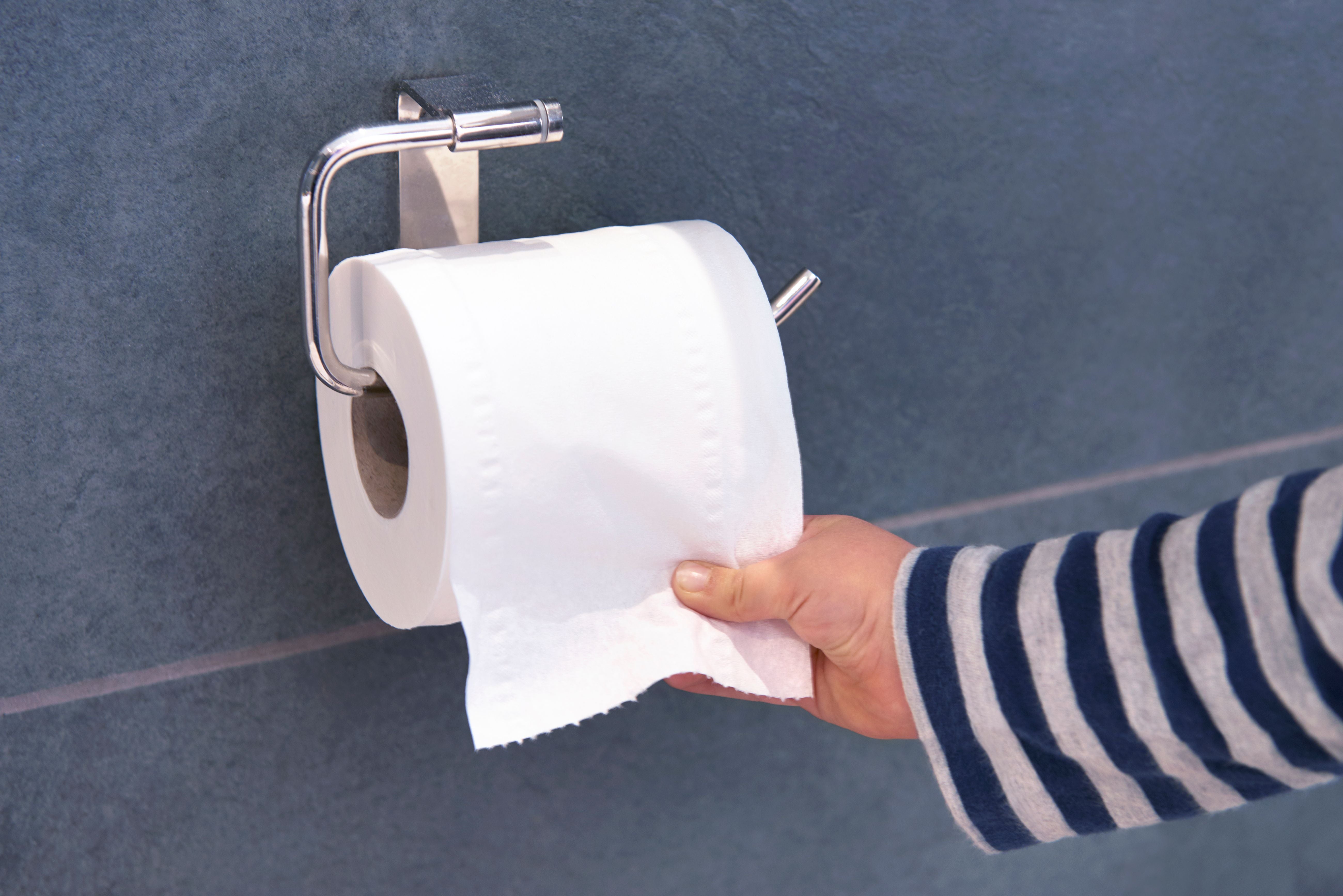Kind zieht Toilettenpapier von einer Rolle an einer Wandhalterung.