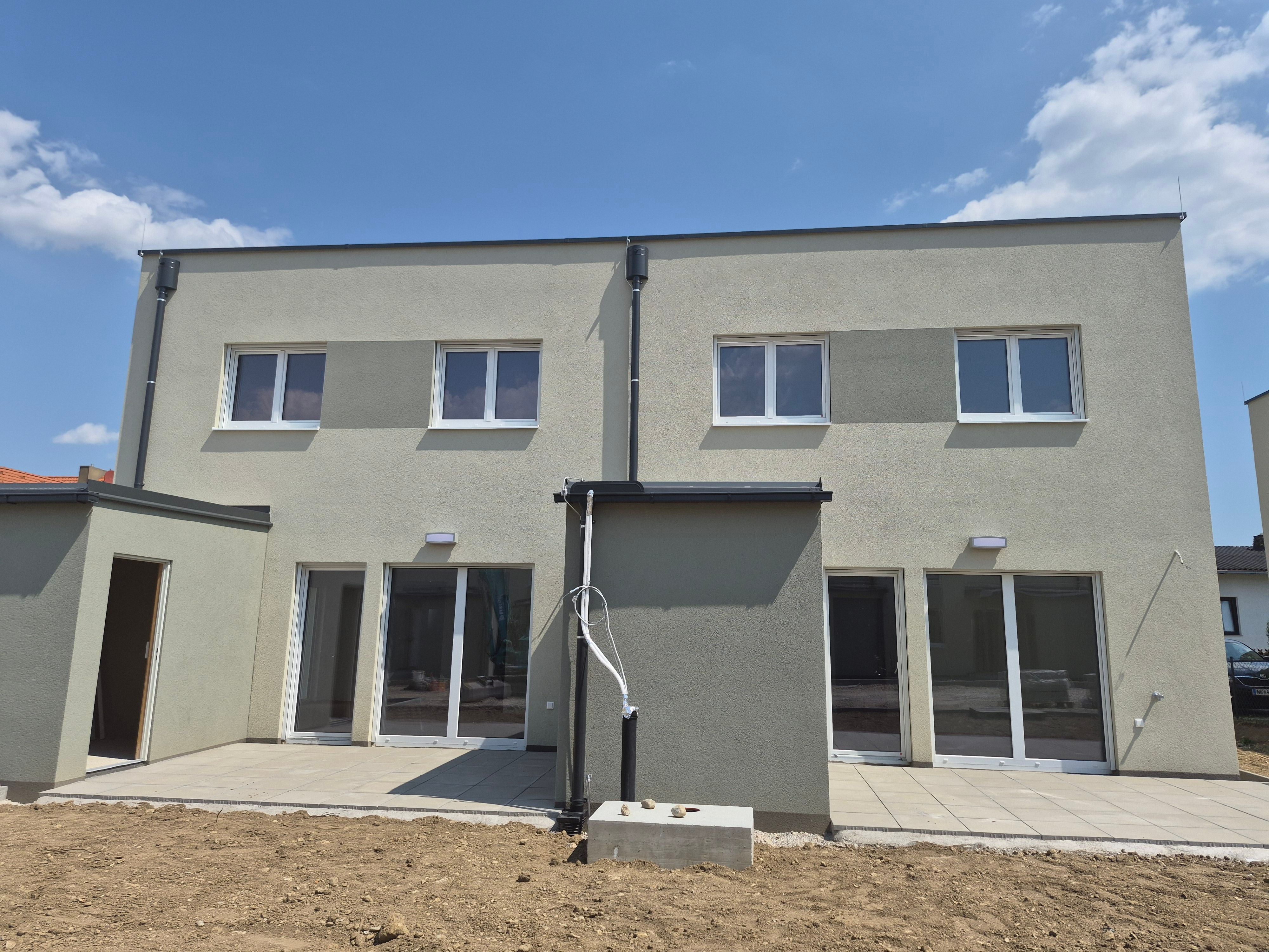 Zweistöckiges modernes Doppelhaus mit großen Fenstern und Terrassen, davor unbepflanzter Garten.
