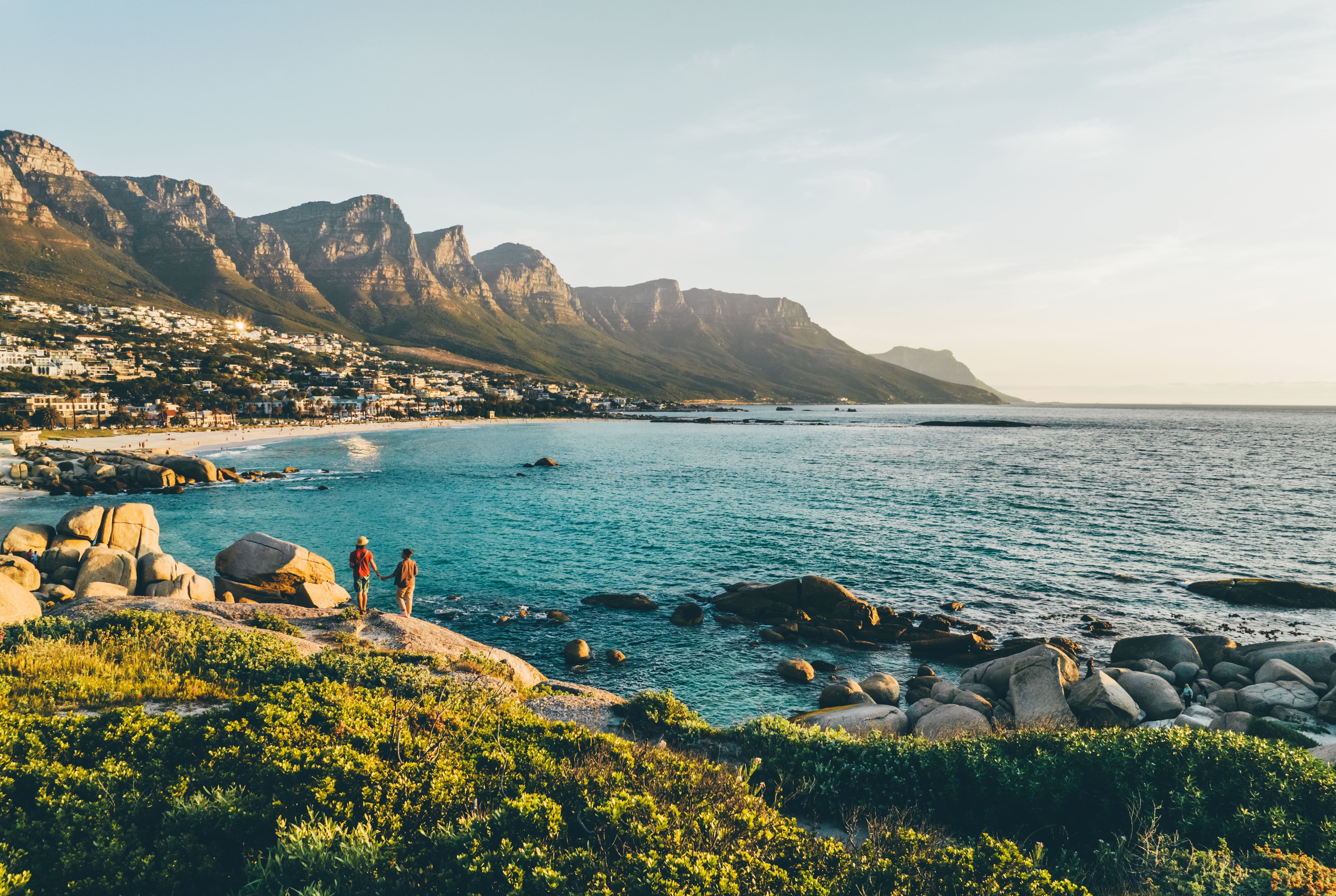 Ein Paar steht auf Felsen und blickt auf das Meer und die Zwölf Apostel in Camps Bay, Kapstadt.