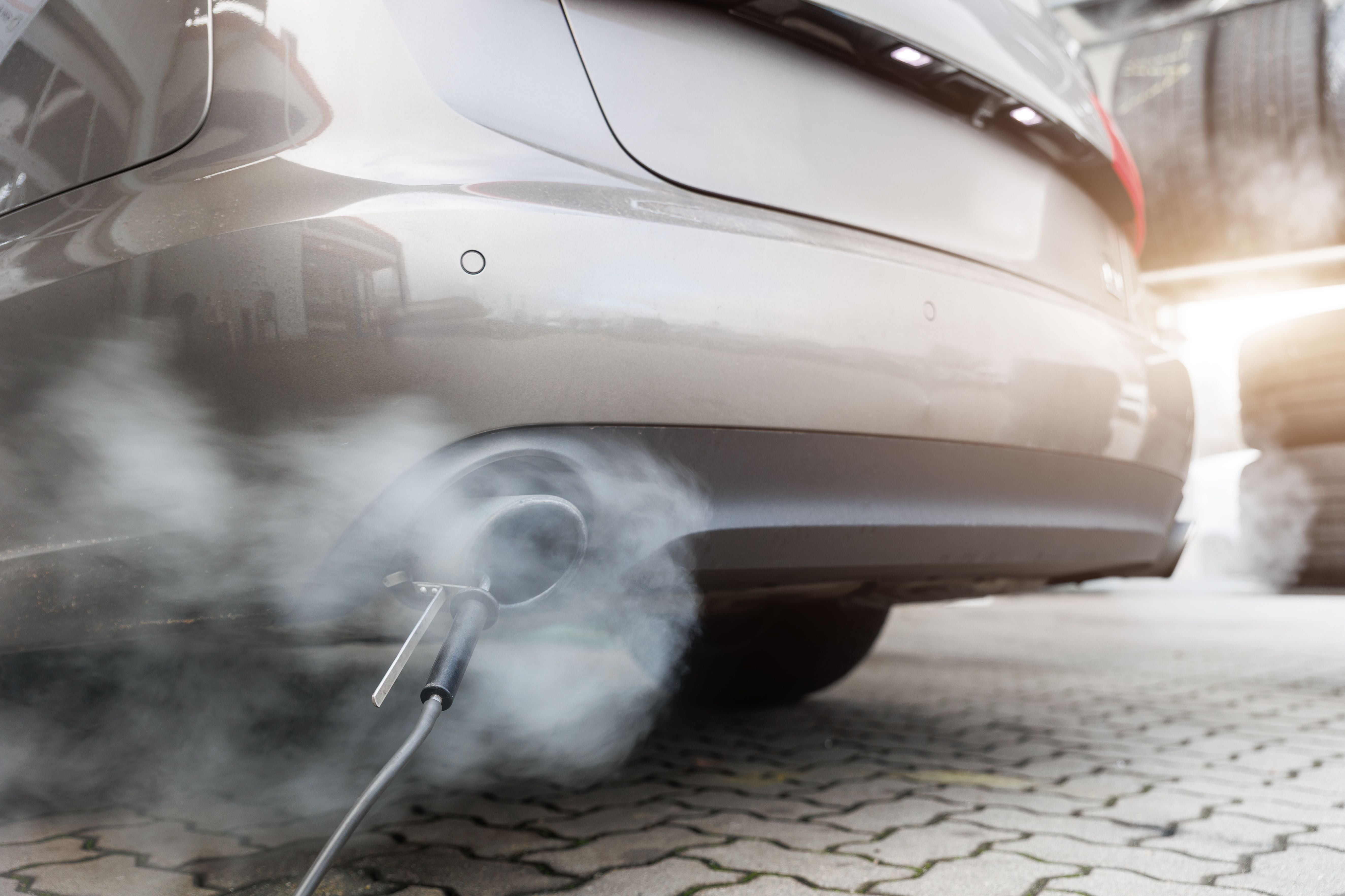 Abgasmessung an einem Autoauspuff mit starker Rauchentwicklung in einer Werkstatt.