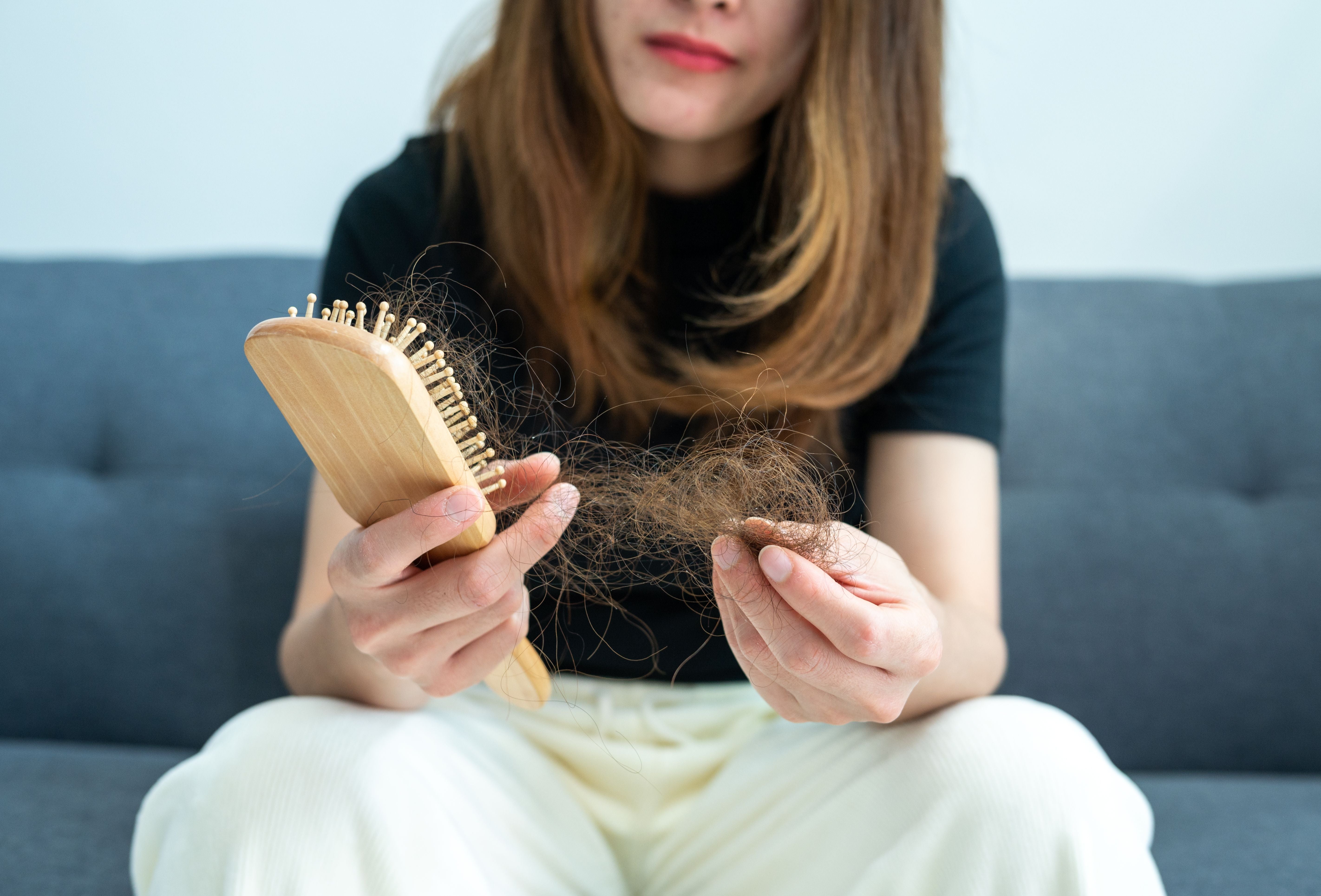 Frau sitzt auf dem Sofa und hält Haarausfall in einer Bürste und in der Hand.