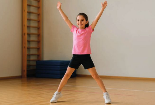 Mädchen in Sportkleidung macht in einer Turnhalle Hampelmänner.