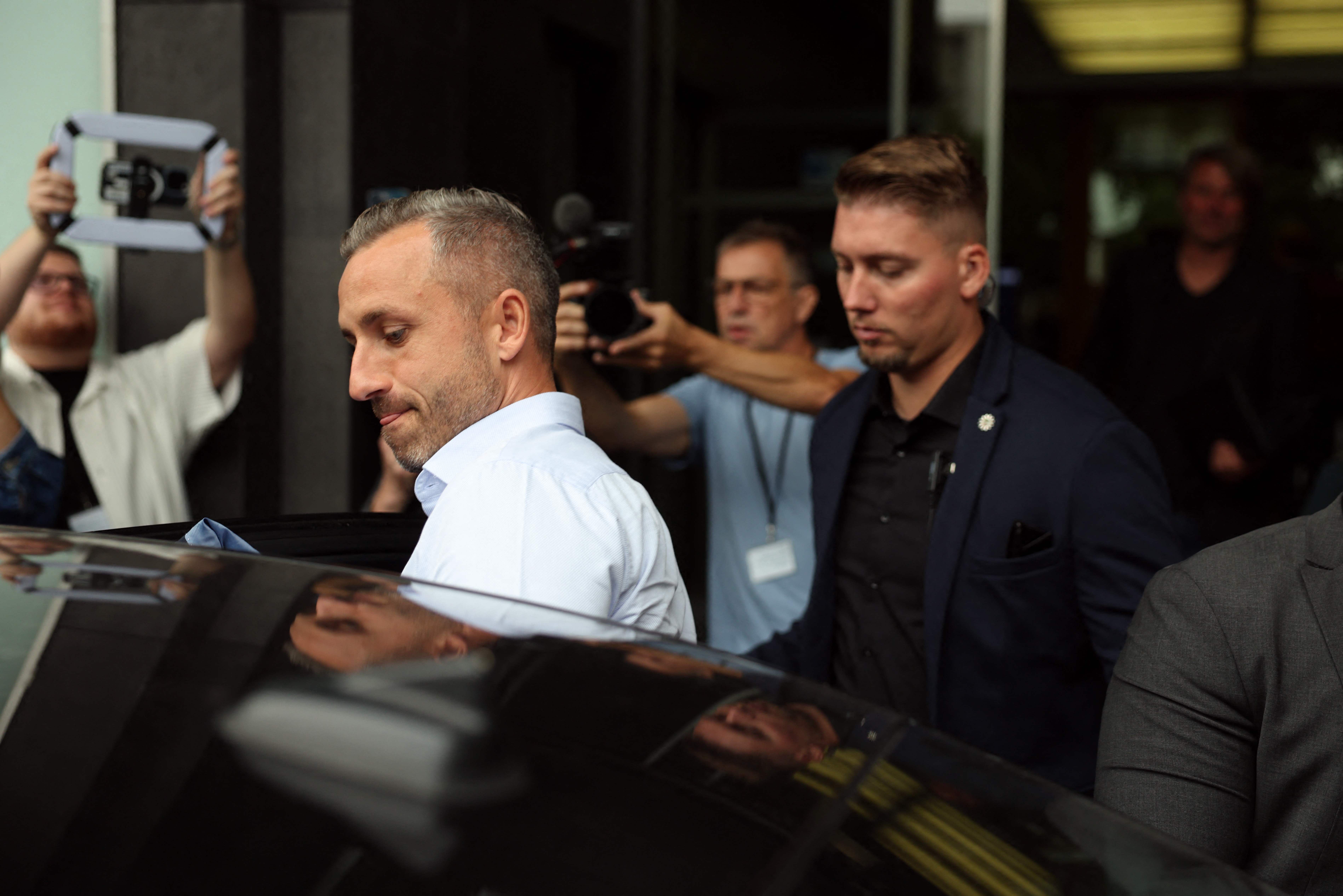 Ein Mann steigt nach einer Pressekonferenz in Berlin in ein Auto, Menschen filmen im Hintergrund.