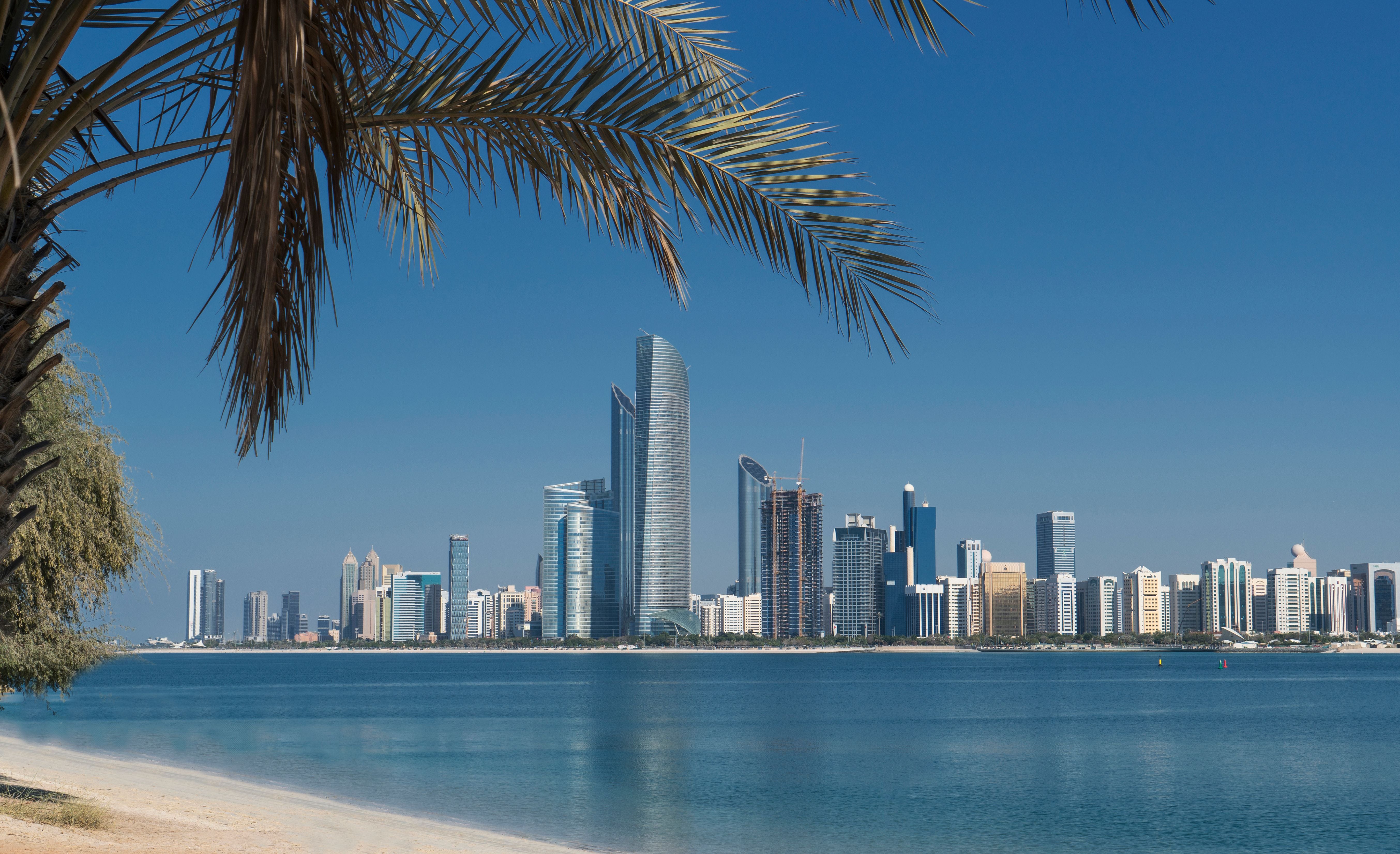 Blick auf die Skyline von Abu Dhabi mit modernen Hochhäusern und Palmen am Wasserufer.