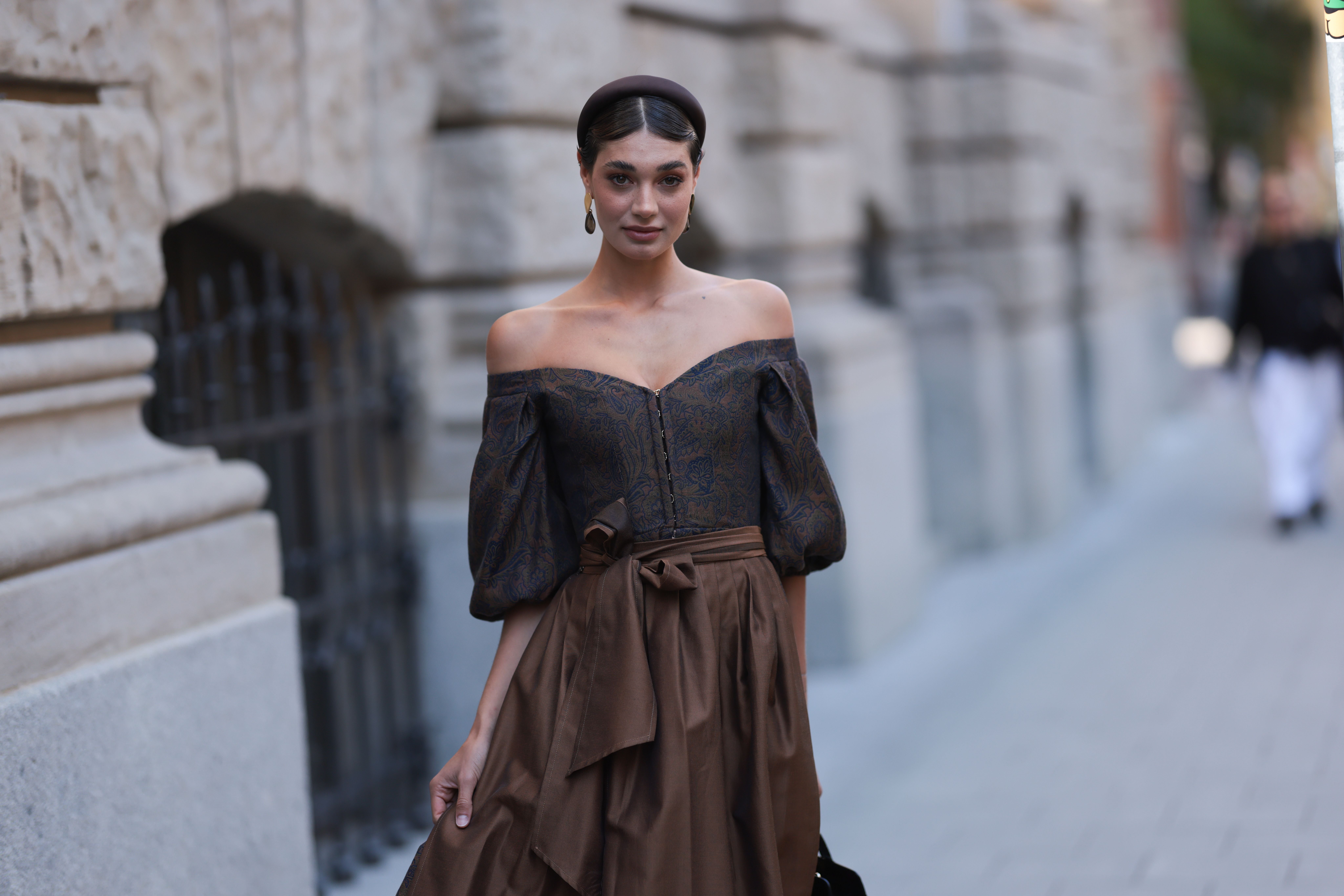 Frau in braunem Dirndl mit Puffärmeln, großem Haarreif und schwarzer Tasche in einer Stadtstraße.
