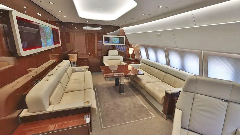 Luxuriöser Innenraum eines Privatjets mit Ledersofas, Bildschirm und Tischen.