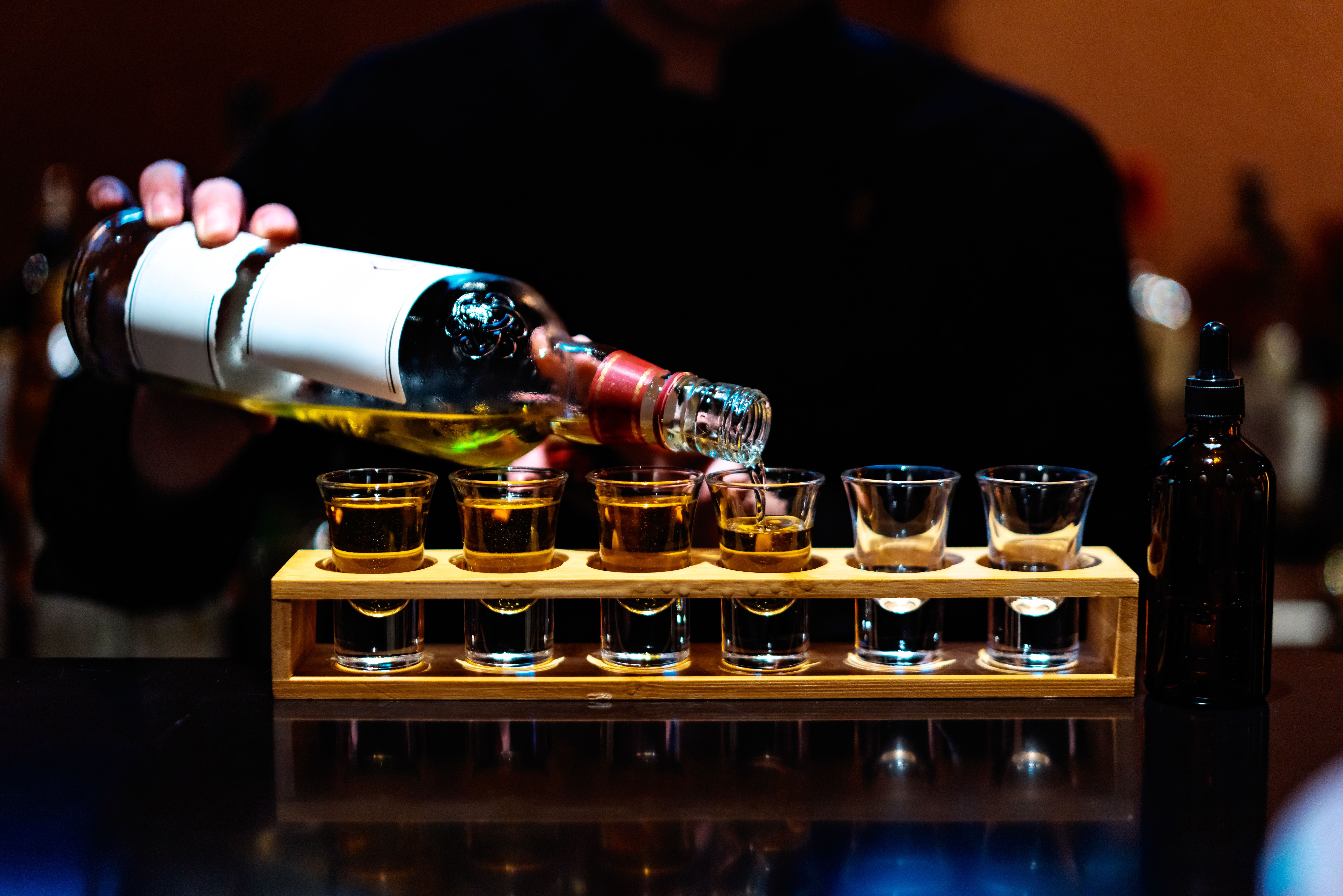 Barkeeper schenkt Whiskey in mehrere Shotgläser auf einem Tresen ein.