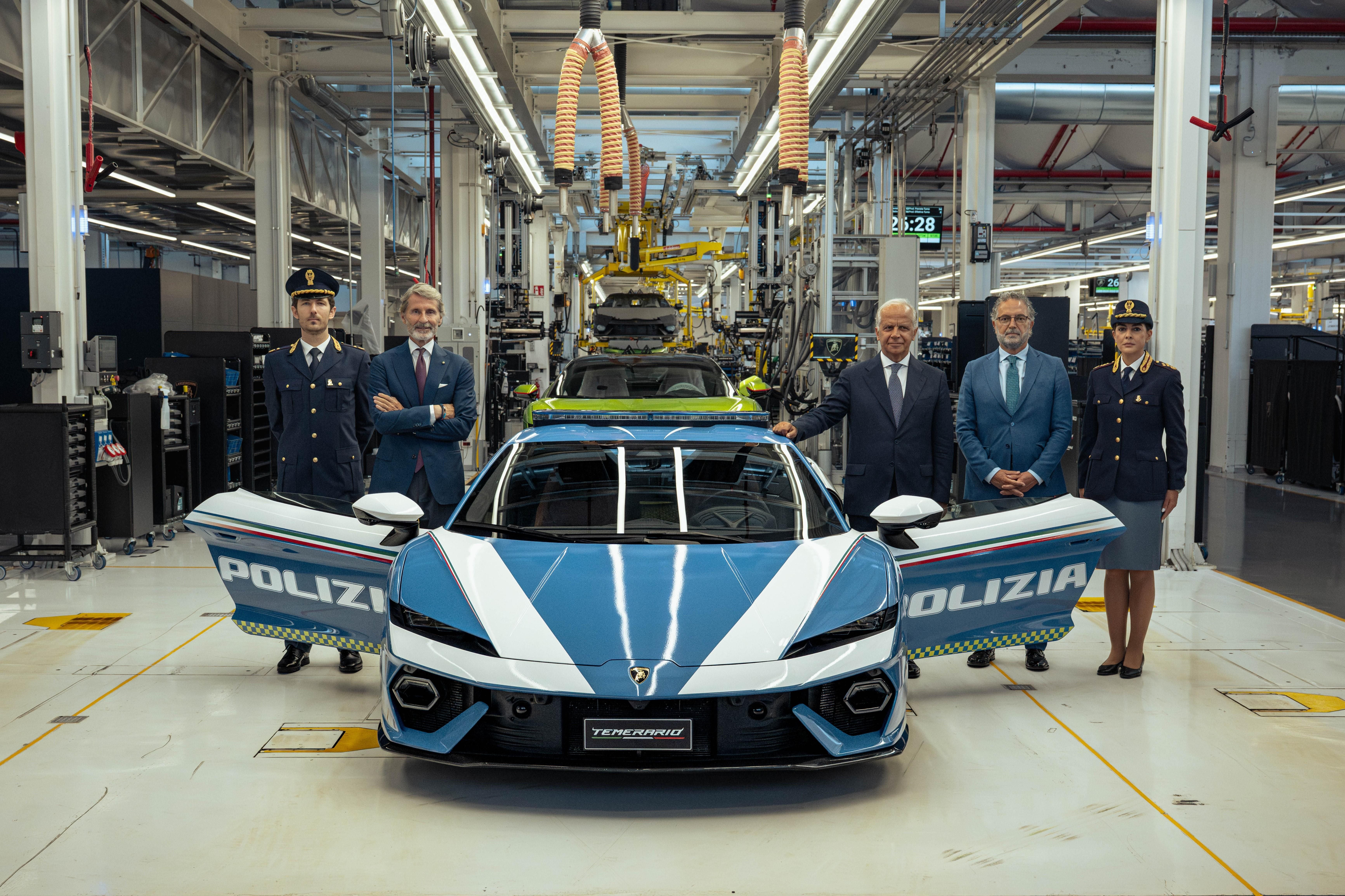 Ein Lamborghini-Polizeiauto steht in einer Fabrikhalle, umgeben von Polizisten und Geschäftsleuten.