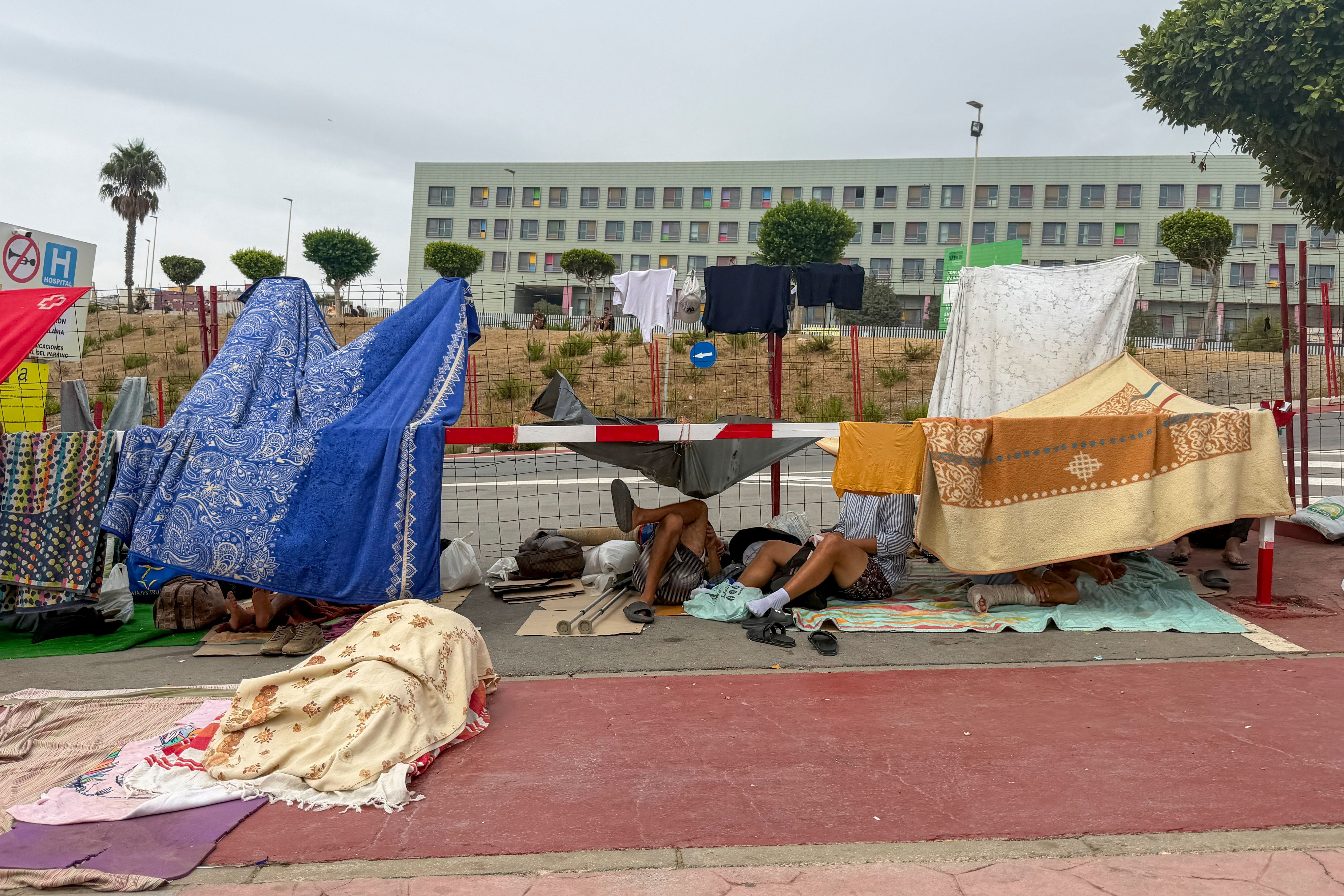 Migranten ruhen unter provisorischen Zelten aus Decken und Tüchern an einer Straße in Ceuta.