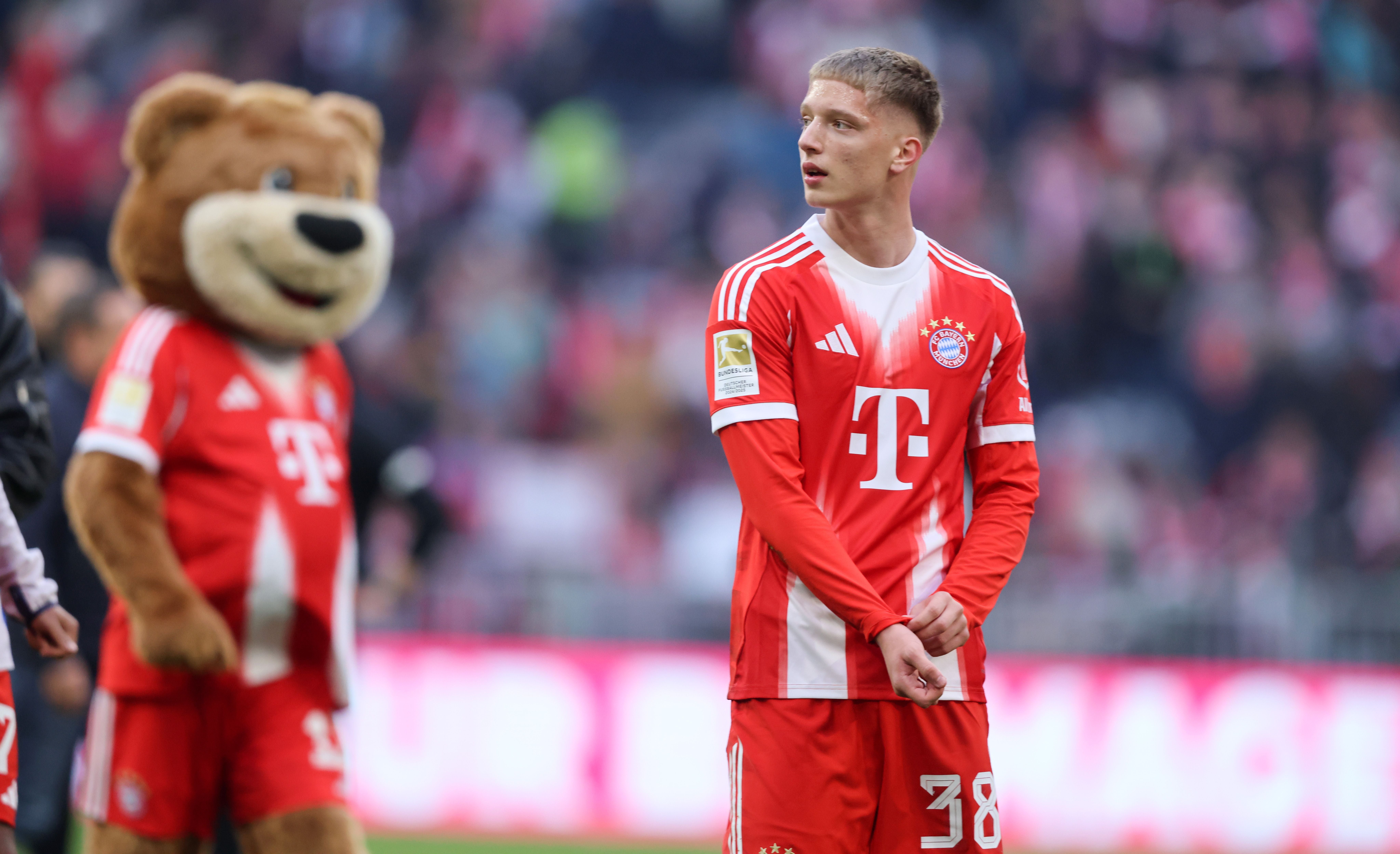 Ein Fußballspieler des FC Bayern steht auf dem Spielfeld, im Hintergrund ein Maskottchen-Bär.