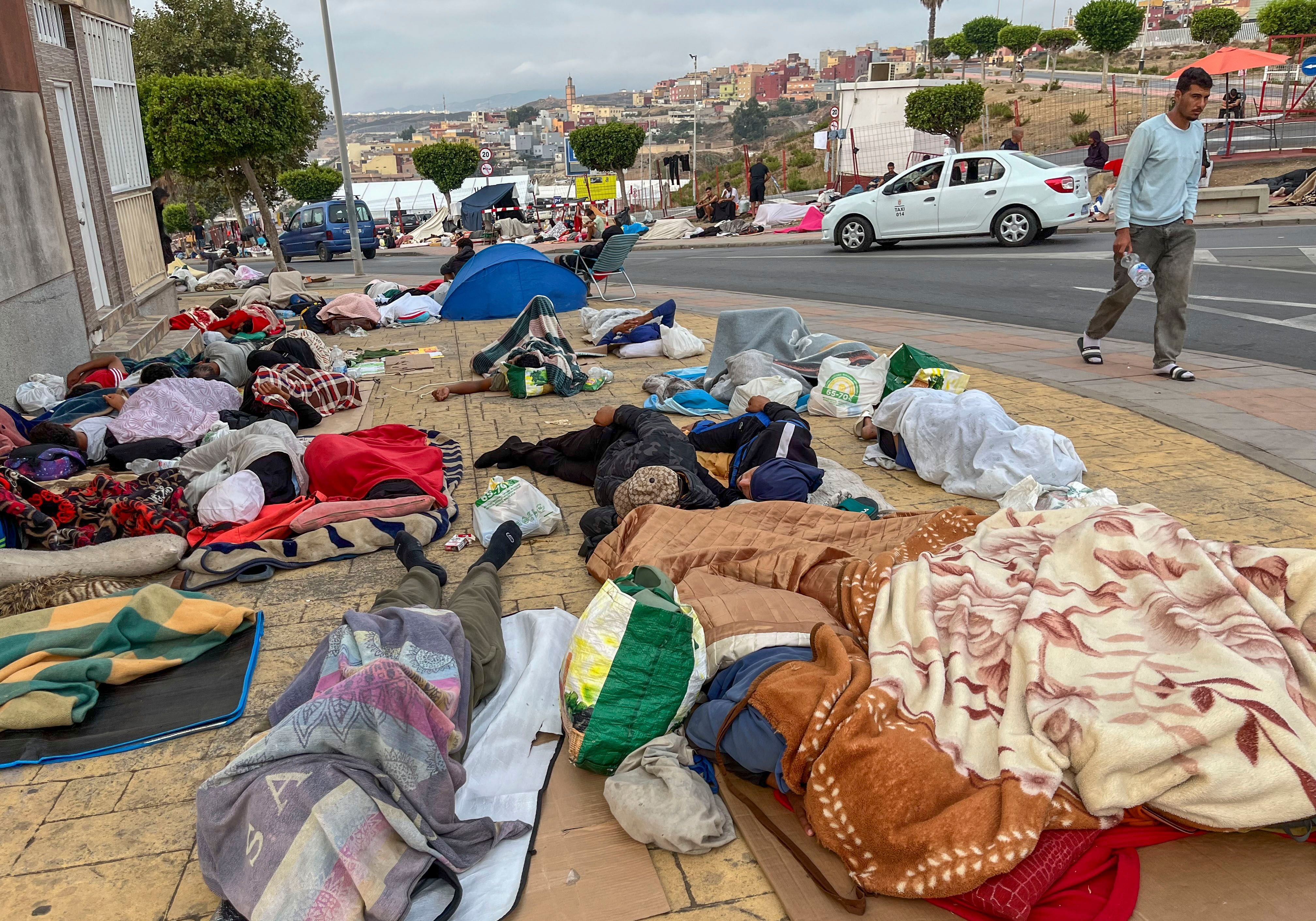 Viele Menschen schlafen mit Decken und Taschen auf dem Bürgersteig einer Straße in Ceuta, Spanien.