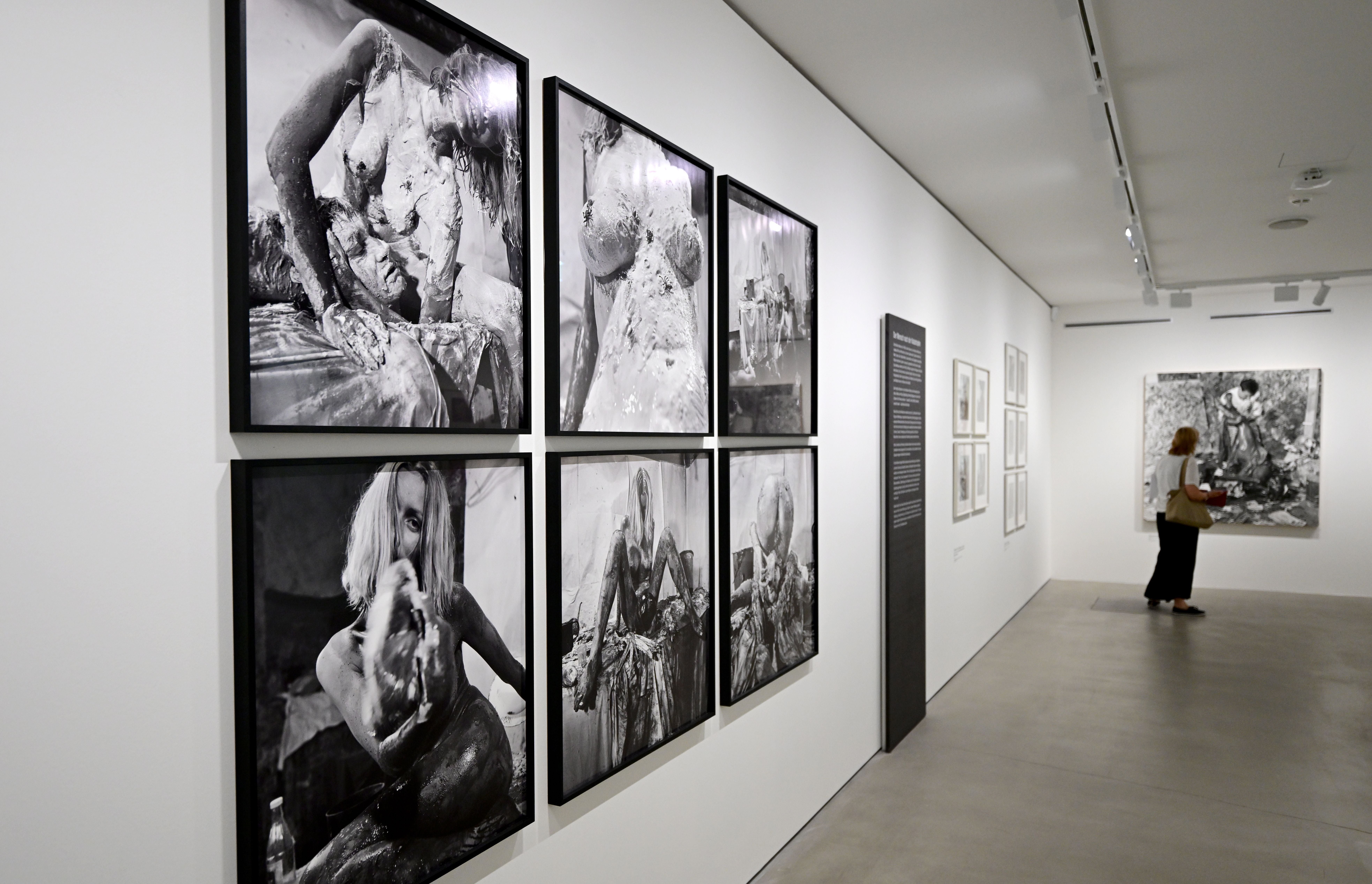 Blick in eine Kunstausstellung mit Schwarz-Weiß-Fotografien an weißen Wänden und einer Besucherin.