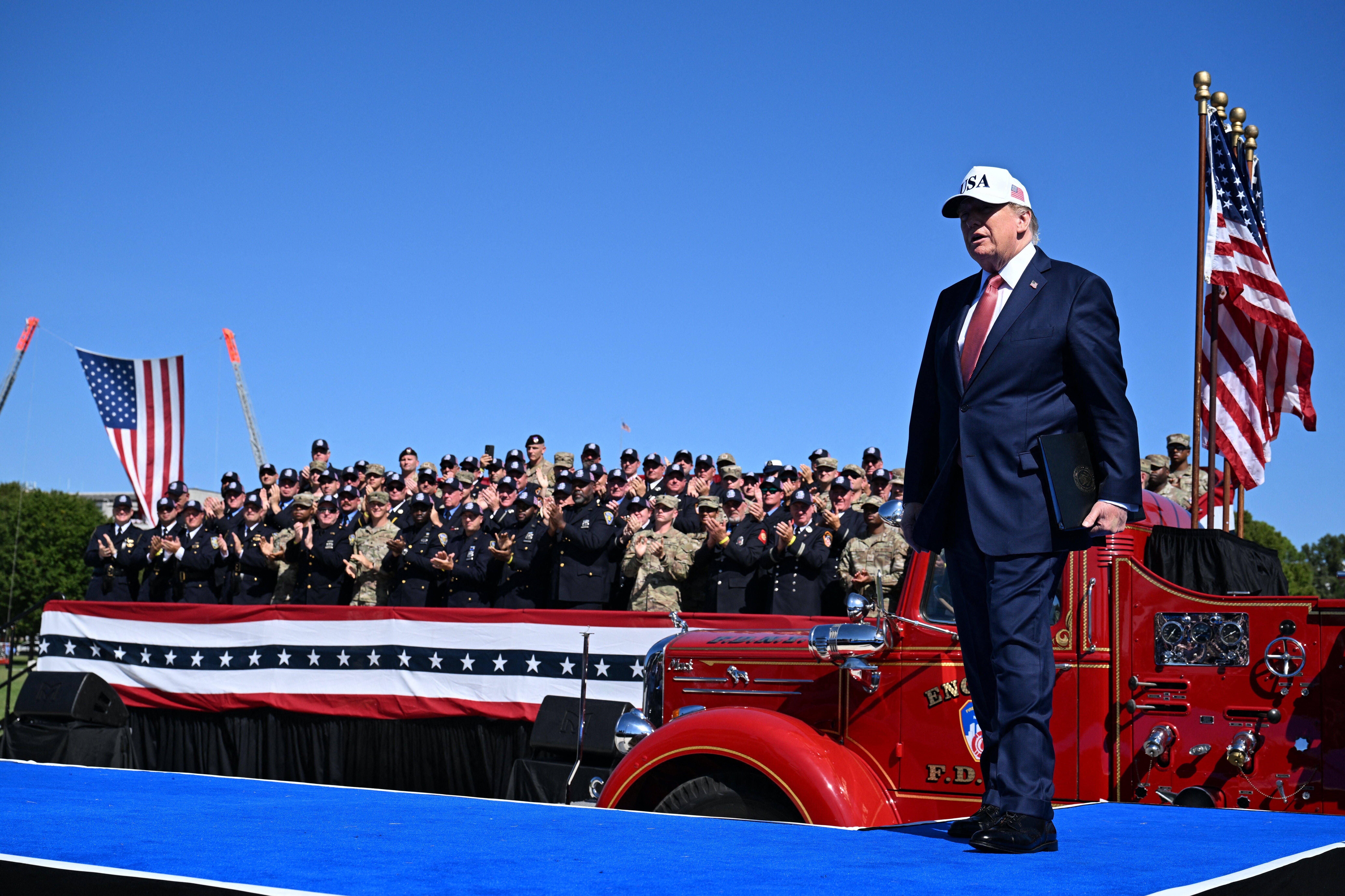 Ein Mann im Anzug läuft an einer US-Flagge vorbei; hinter ihm applaudiert eine Gruppe Uniformierter.