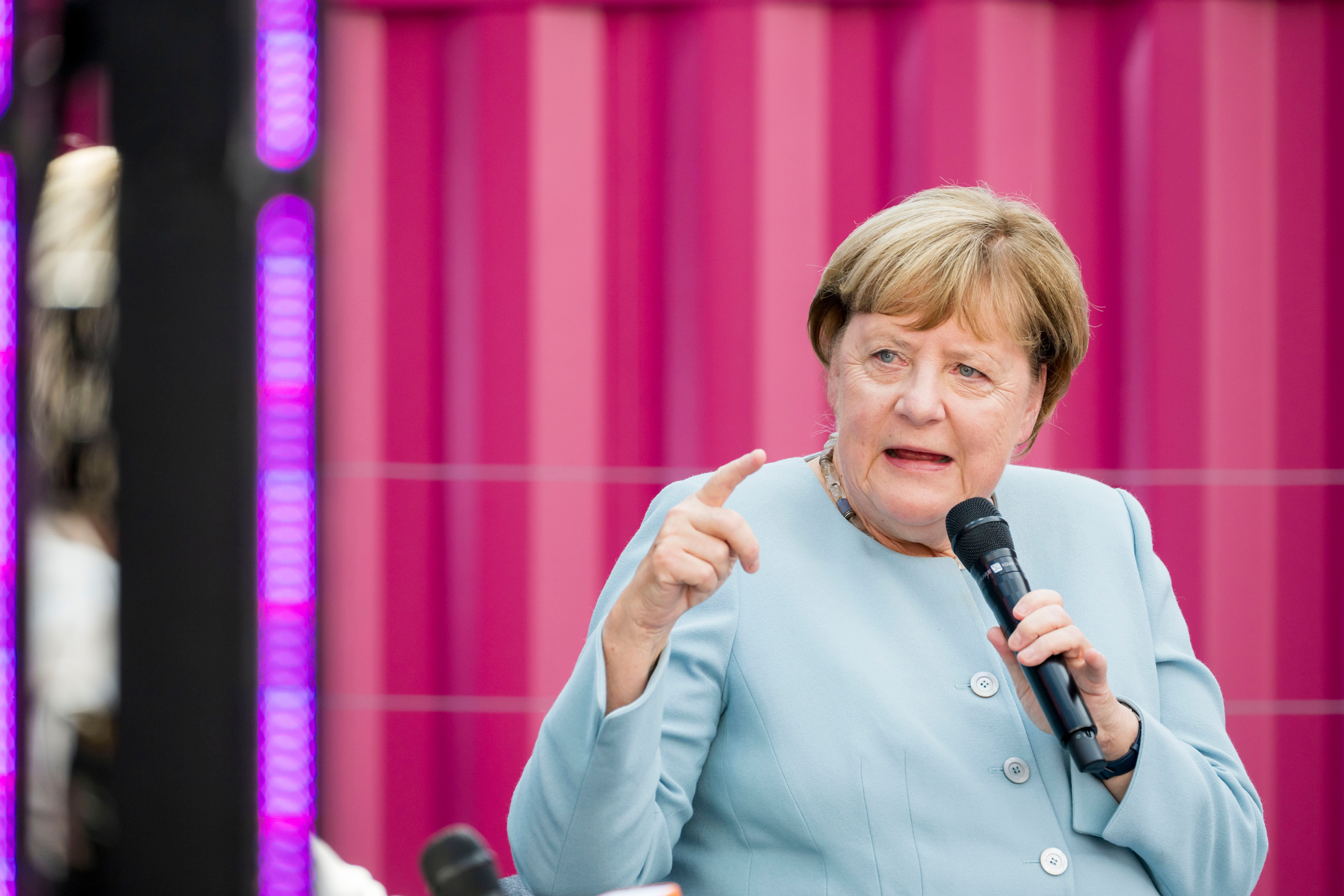 Eine Frau im hellblauen Blazer spricht mit Mikrofon vor pinkem Hintergrund auf einer Bühne.
