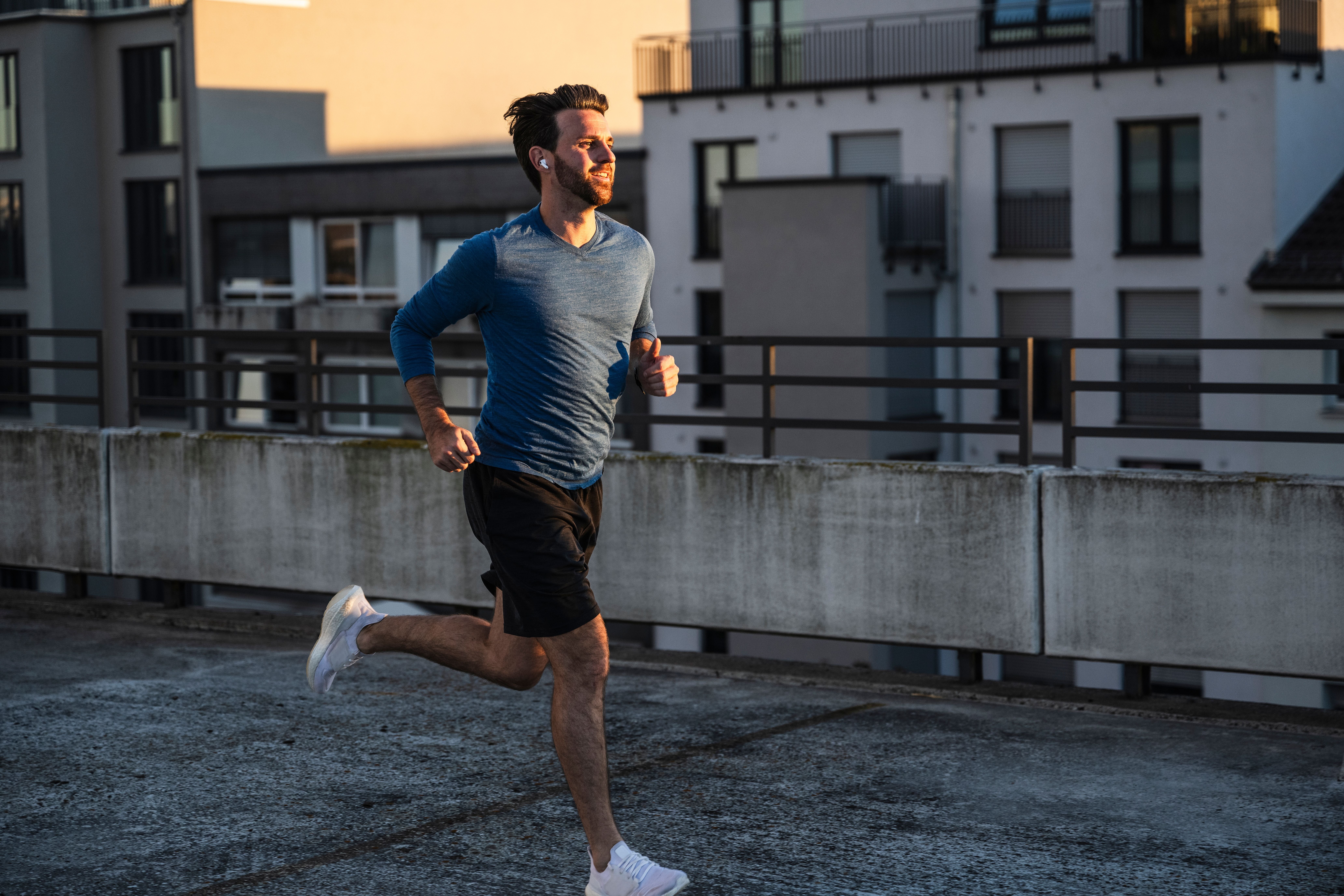 Ein Mann joggt bei Sonnenuntergang auf einer Dachterrasse vor einem Wohngebäude.