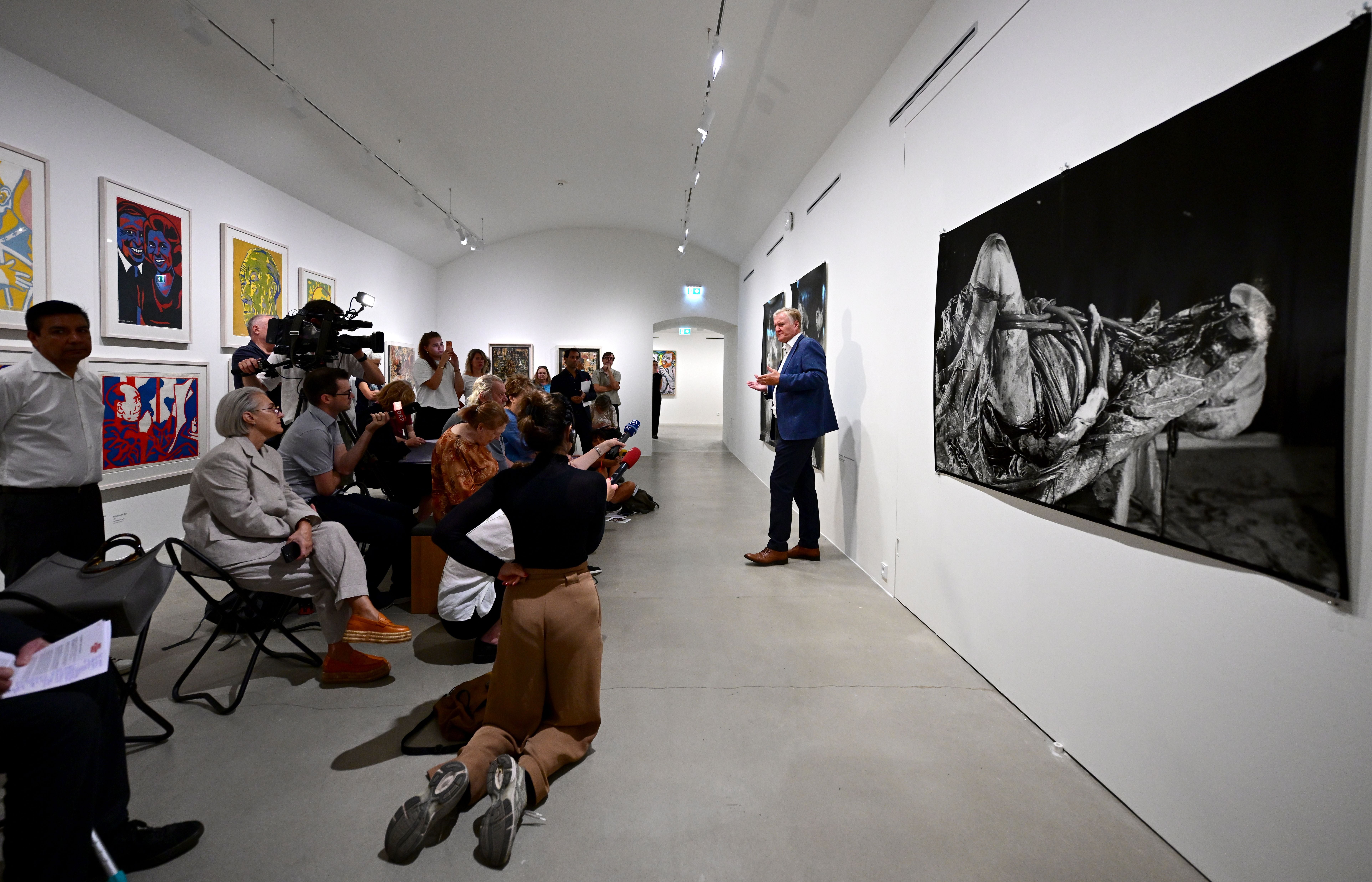 Presseführung in einer Kunstgalerie mit mehreren Besuchern und einem Redner vor modernen Kunstwerken.