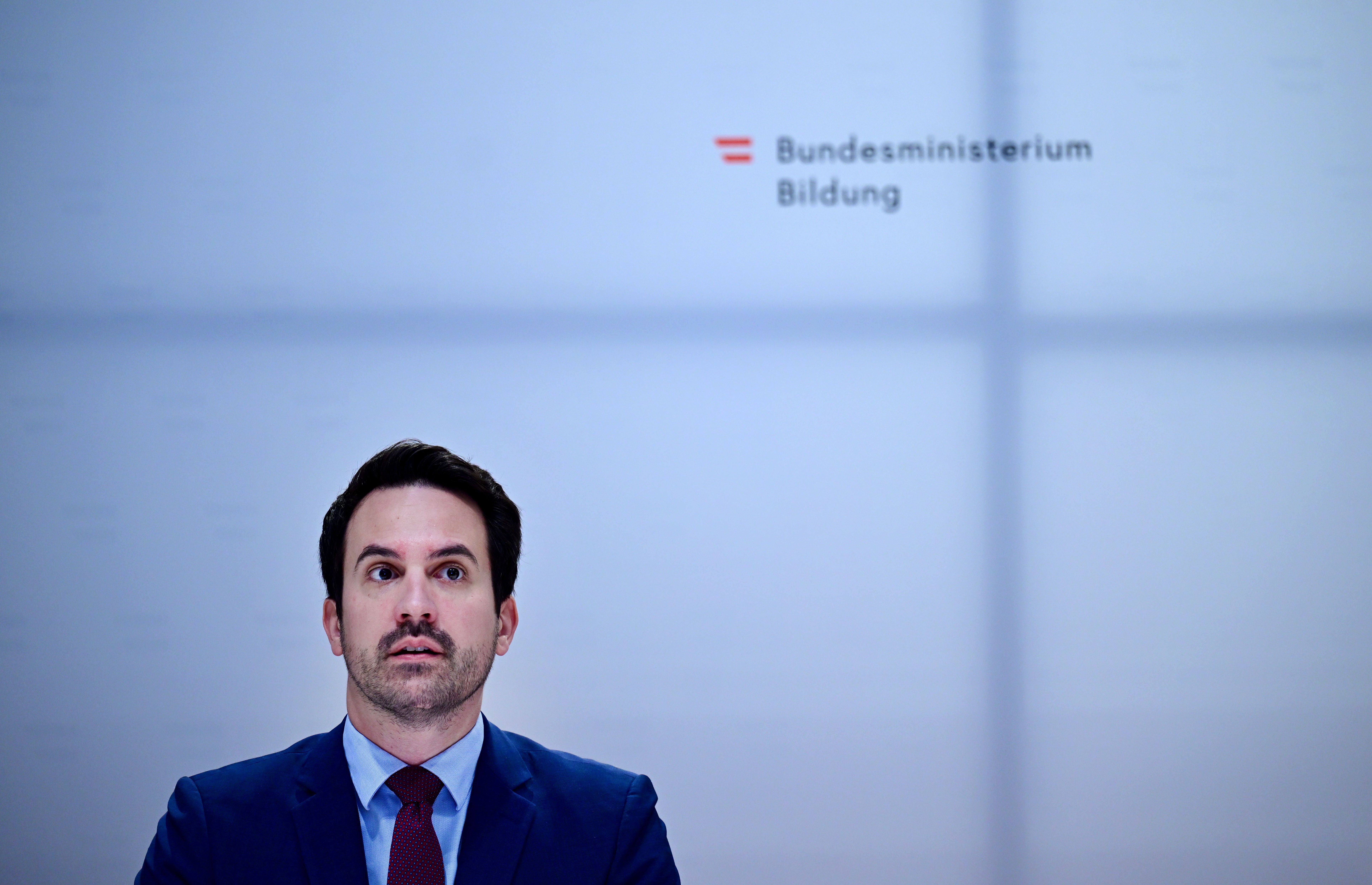 Ein Mann im Anzug vor einer Wand mit dem Logo des Bundesministeriums für Bildung.