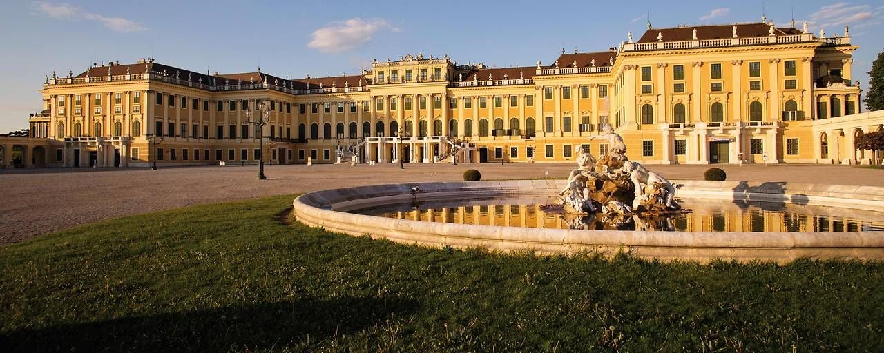 Das Schloss Schönbrunn mit Springbrunnen bei Sonnenschein und blauem Himmel.