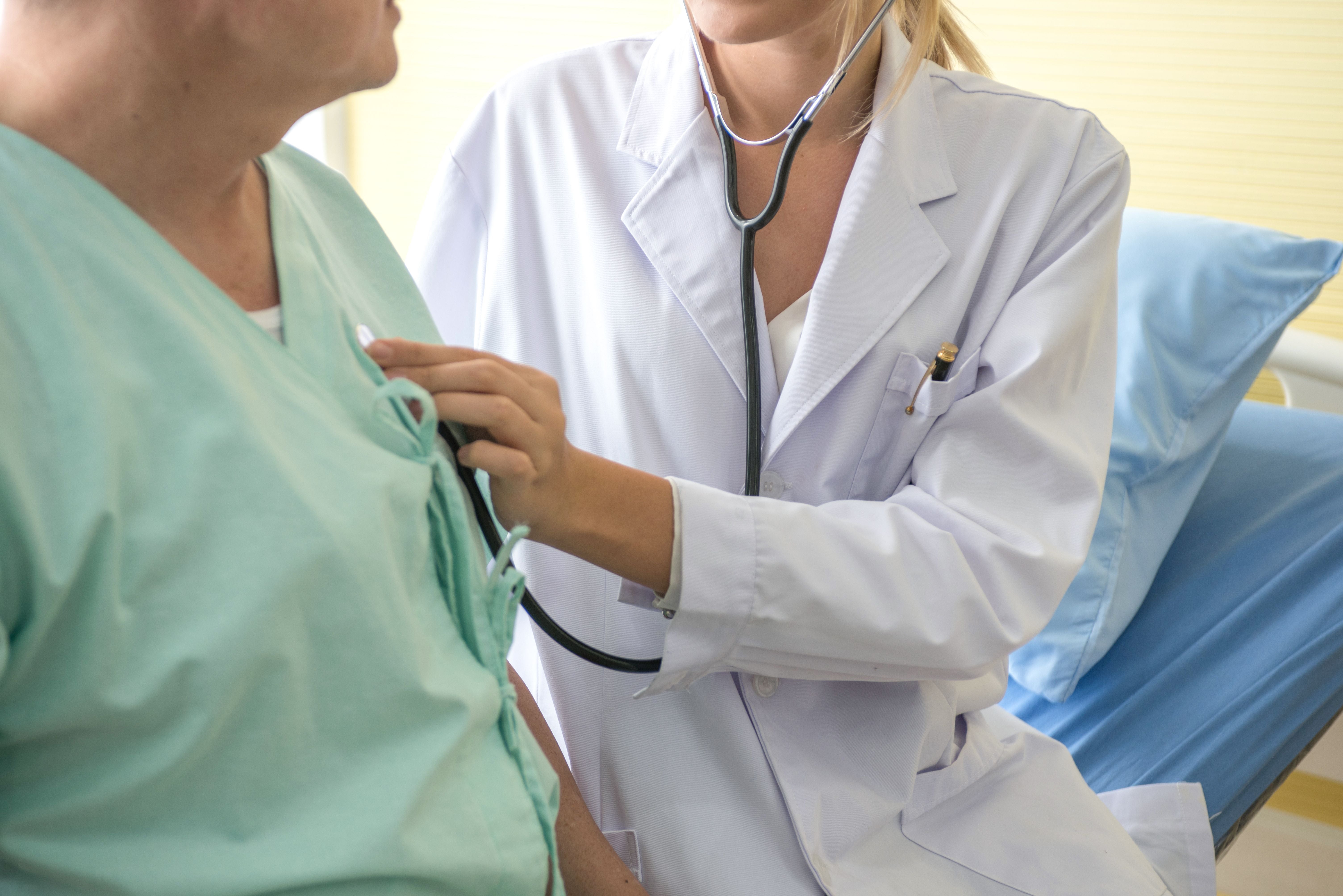 Ärztin untersucht Patienten mit Stethoskop am Brustkorb im Krankenzimmer.
