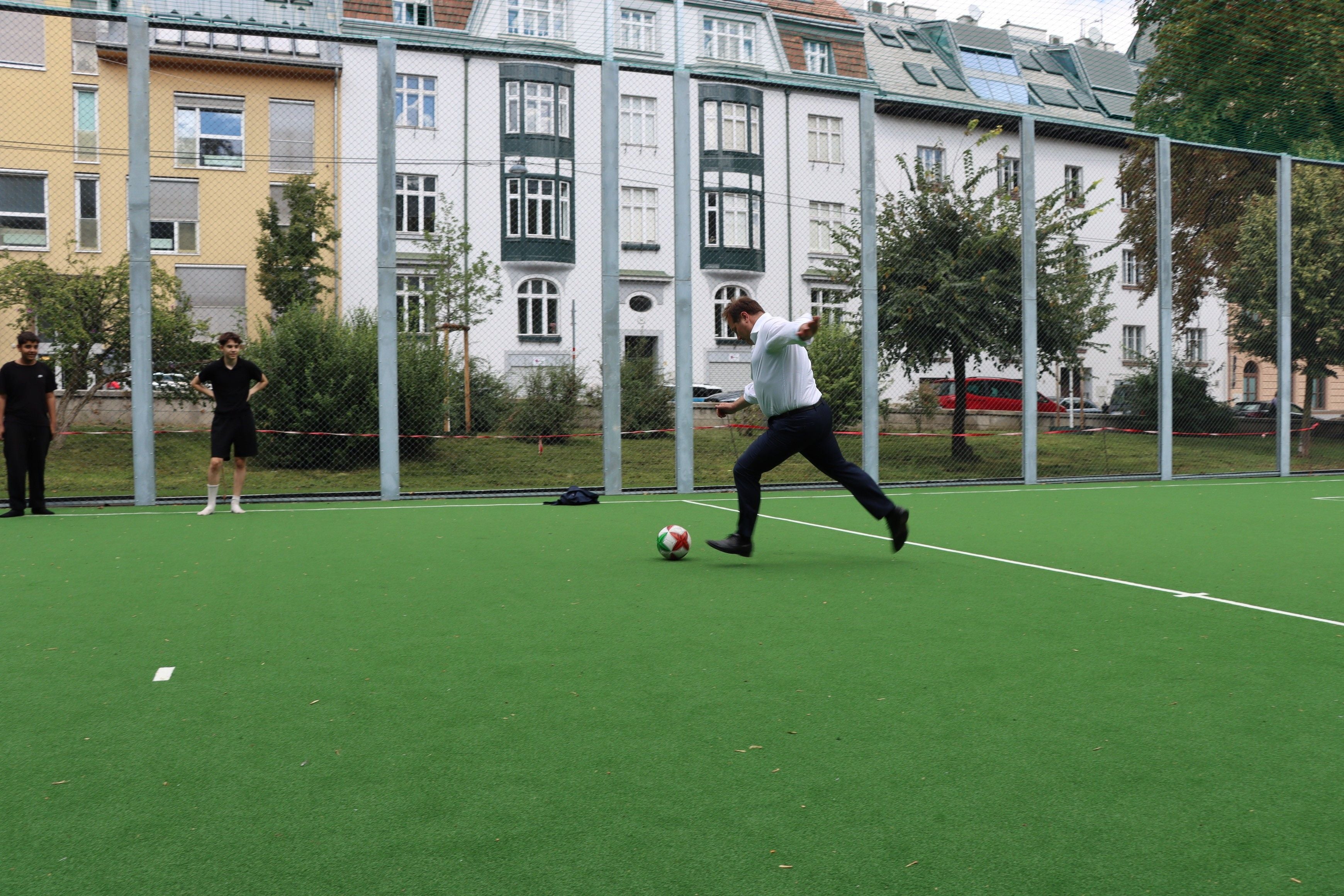 Mann im Anzug schießt einen Ball auf einem Fußballplatz im Heiligenstädter Park.