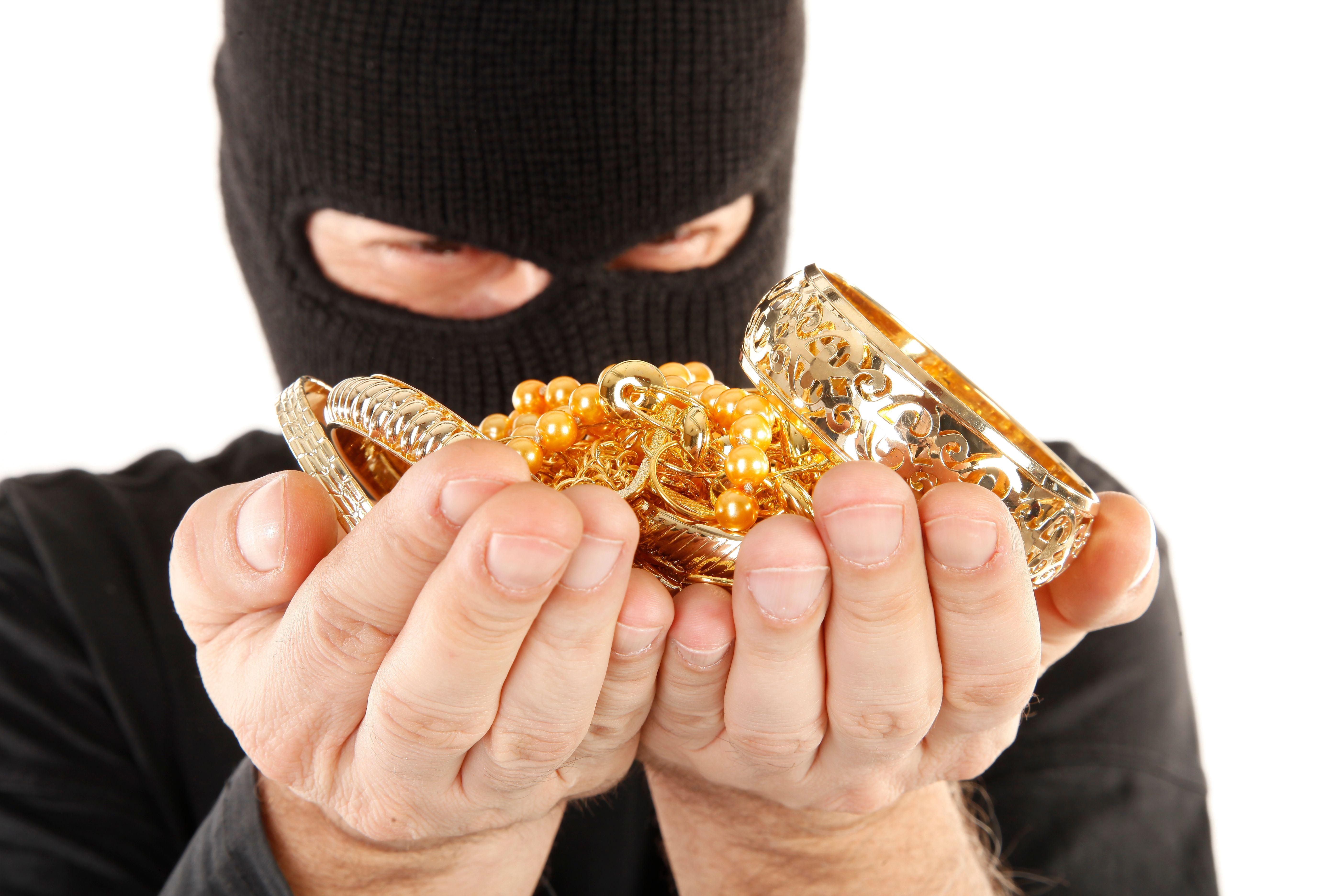 Maskierter Mann hält gestohlenen Goldschmuck in den Händen.