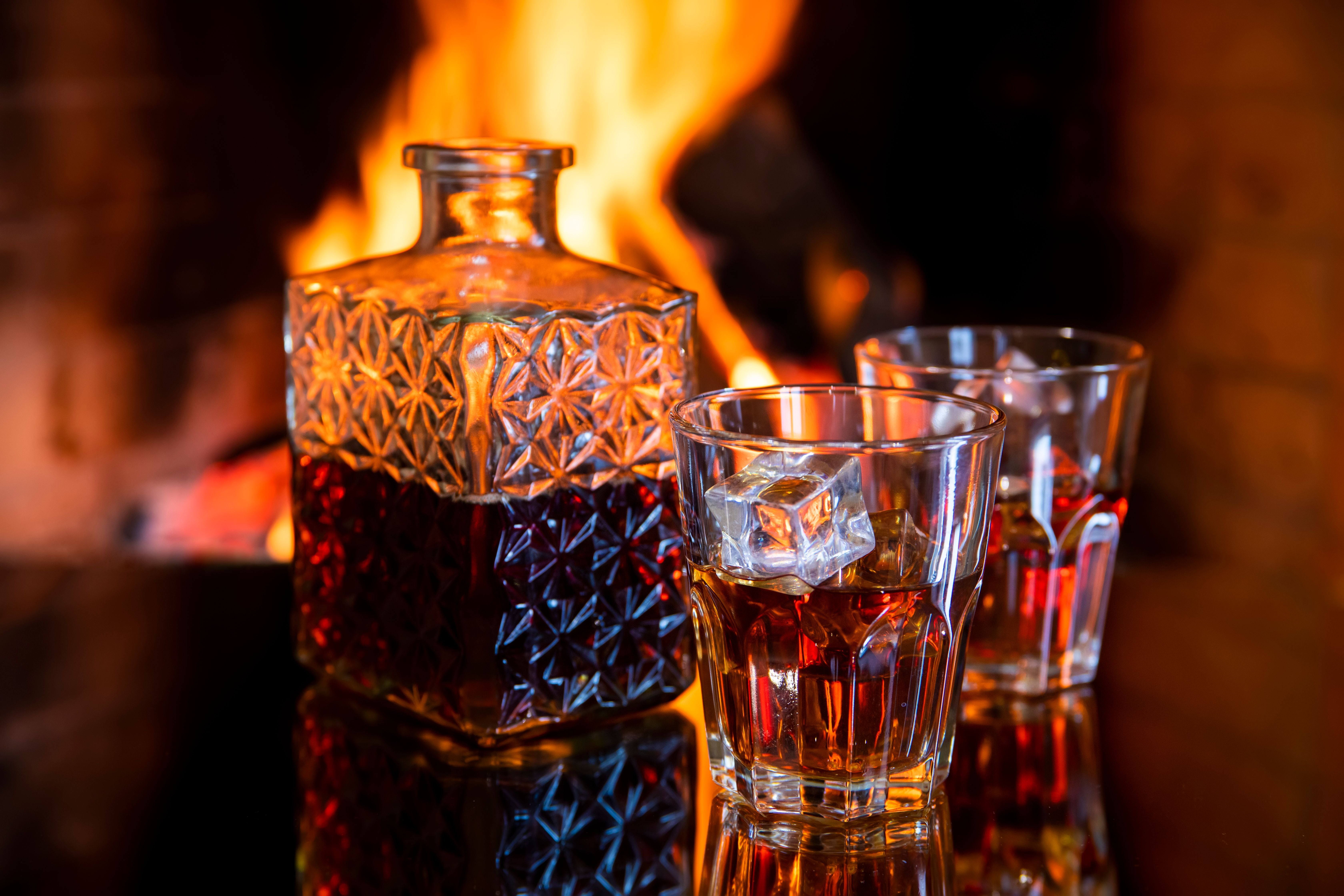 Karaffe und zwei Whiskygläser mit Eis vor einem prasselnden Kaminfeuer.