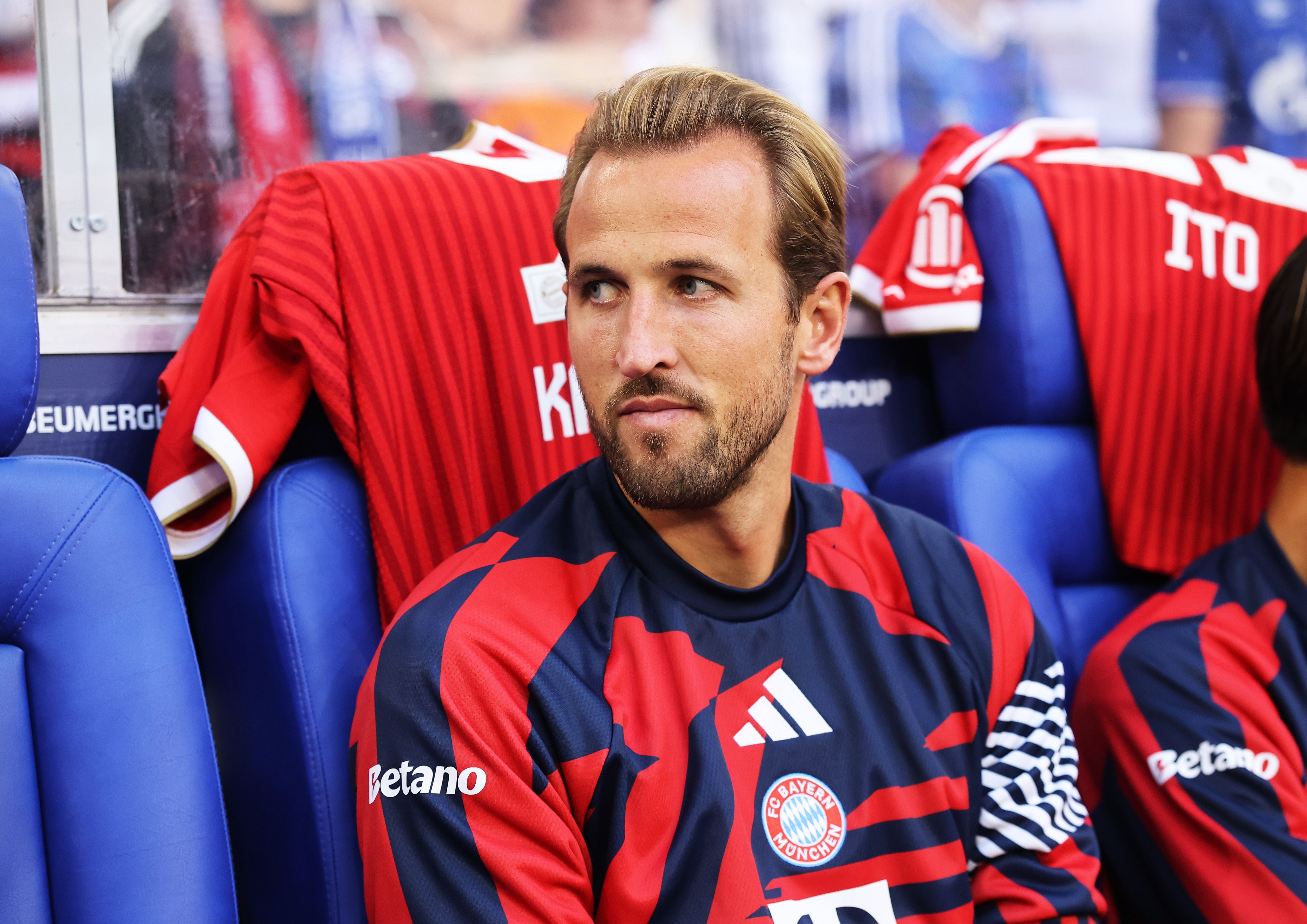 Ein FC-Bayern-Spieler sitzt im rot-blauen Trikot auf der Ersatzbank im Stadion.