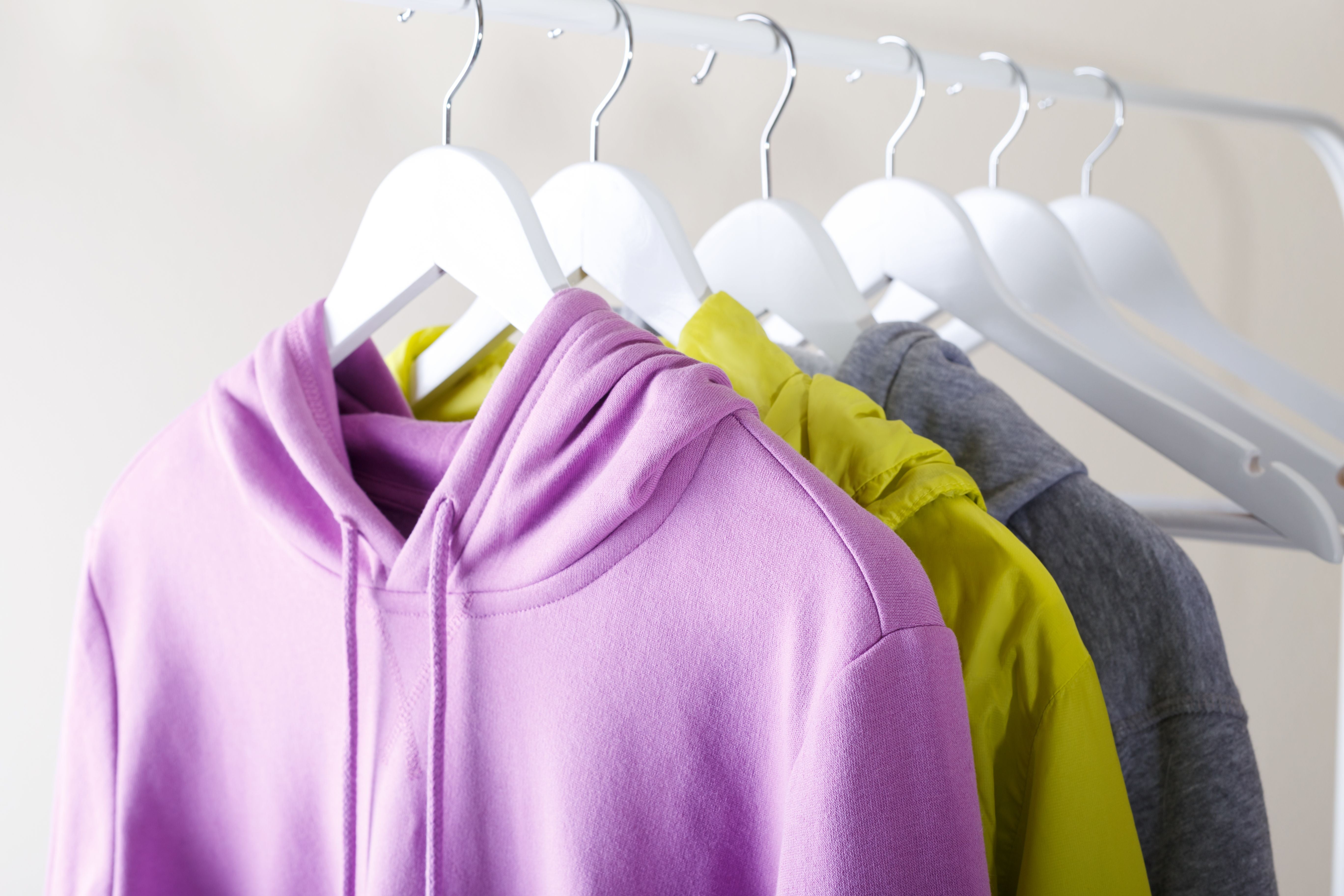 Mehrere bunte Hoodies und T-Shirts hängen auf weißen Kleiderbügeln an einer Kleiderstange.