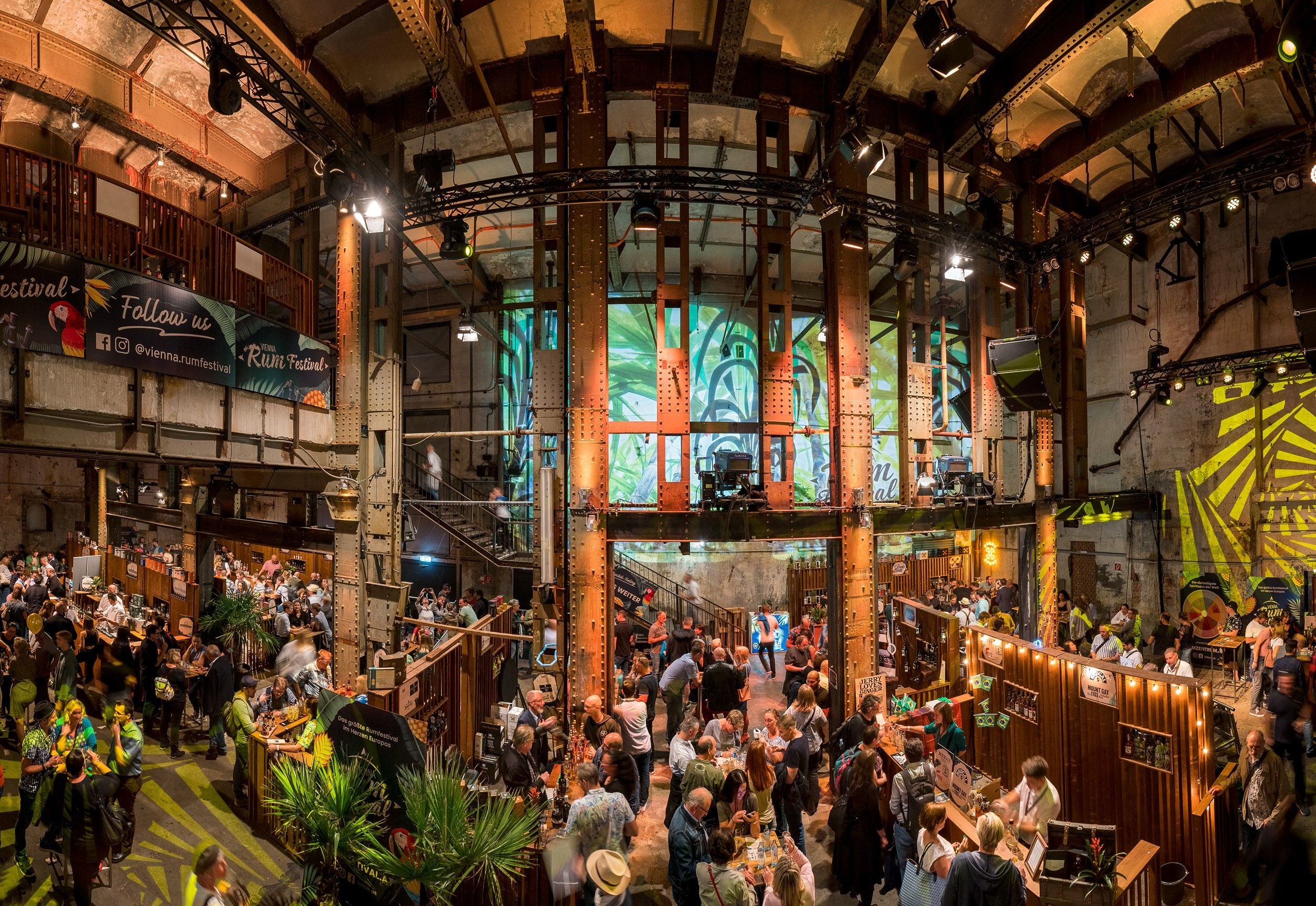 Viele Menschen besuchen ein Rumfestival in einer großen, stimmungsvoll beleuchteten Halle.