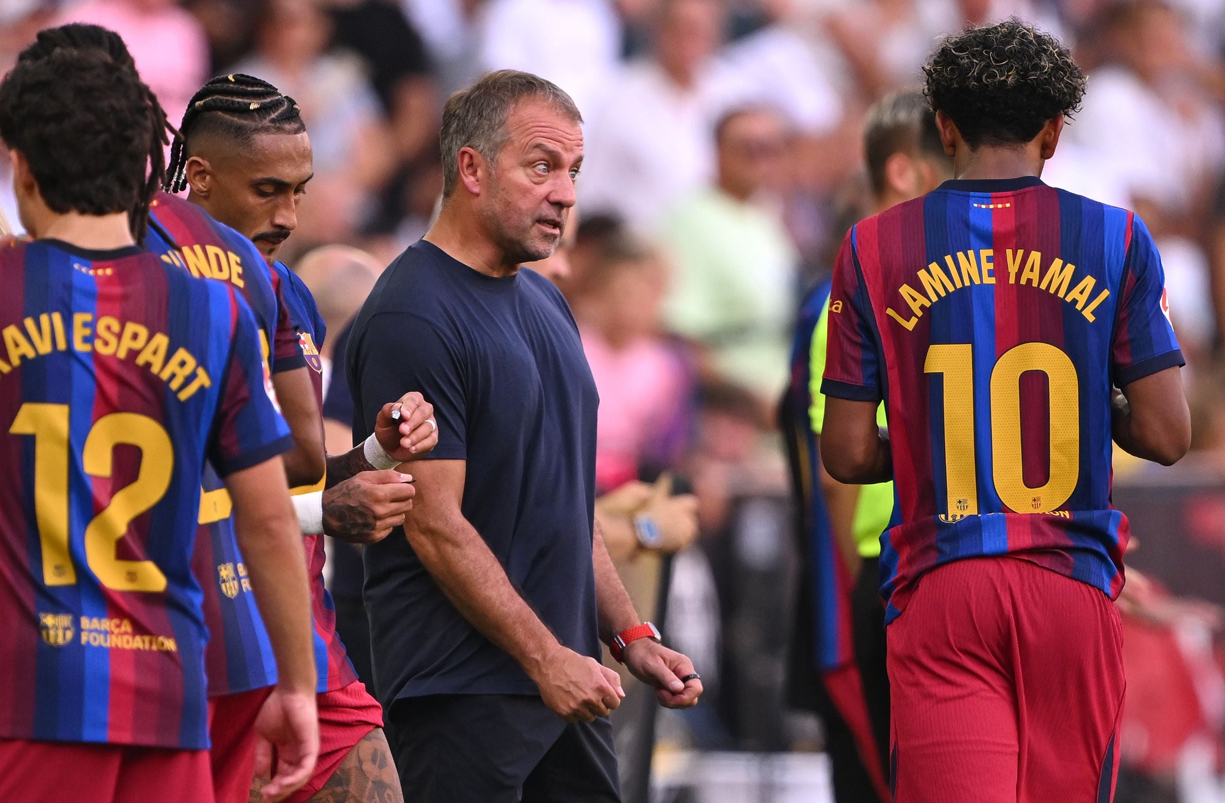 Barca-Cheftrainer Hansi Flick im dunklen T-Shirt im Gespräch mit seinen Spielern um Lamine Yamal und Raphinha.
