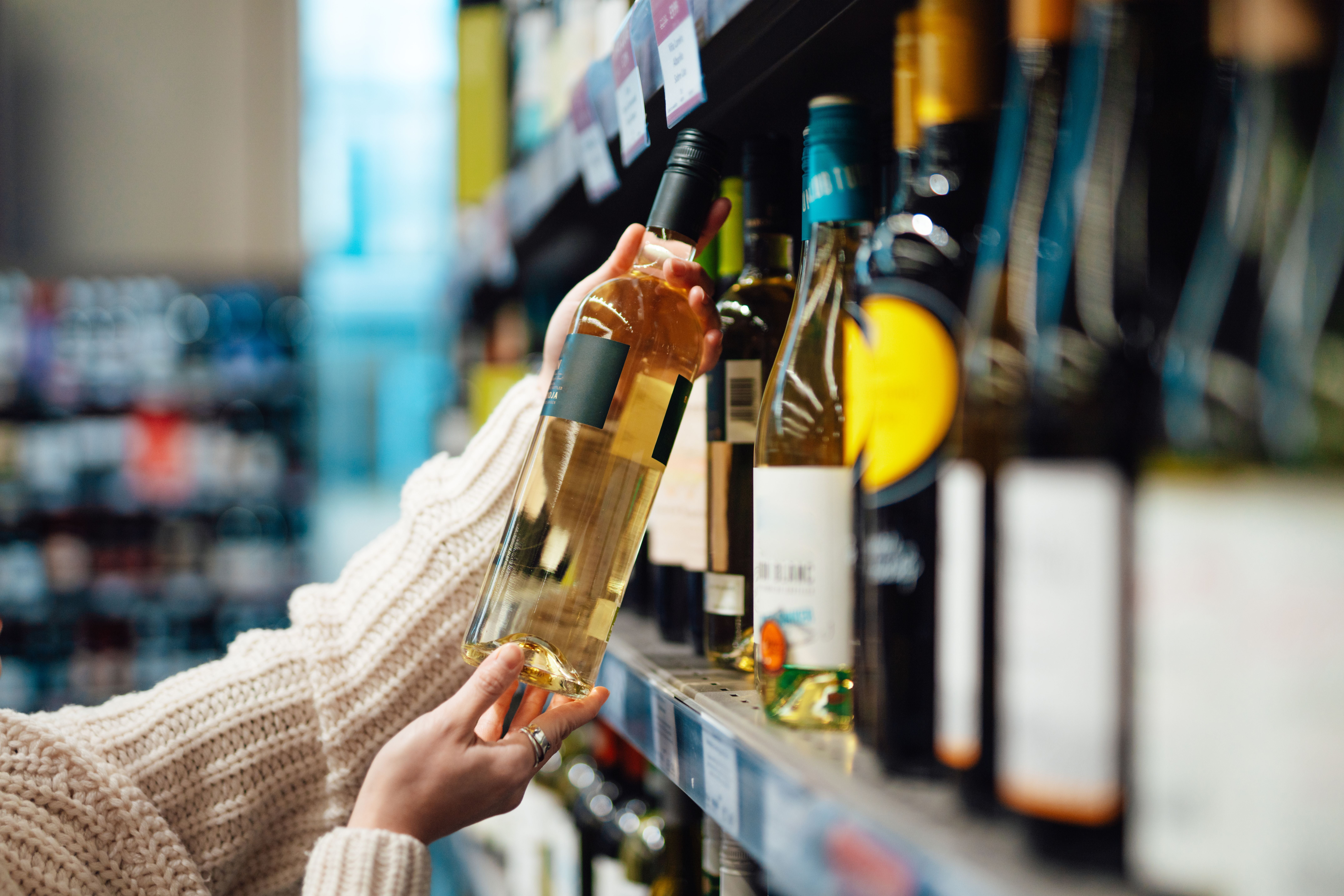Frau nimmt eine Flasche Weißwein aus dem Regal im Supermarkt.