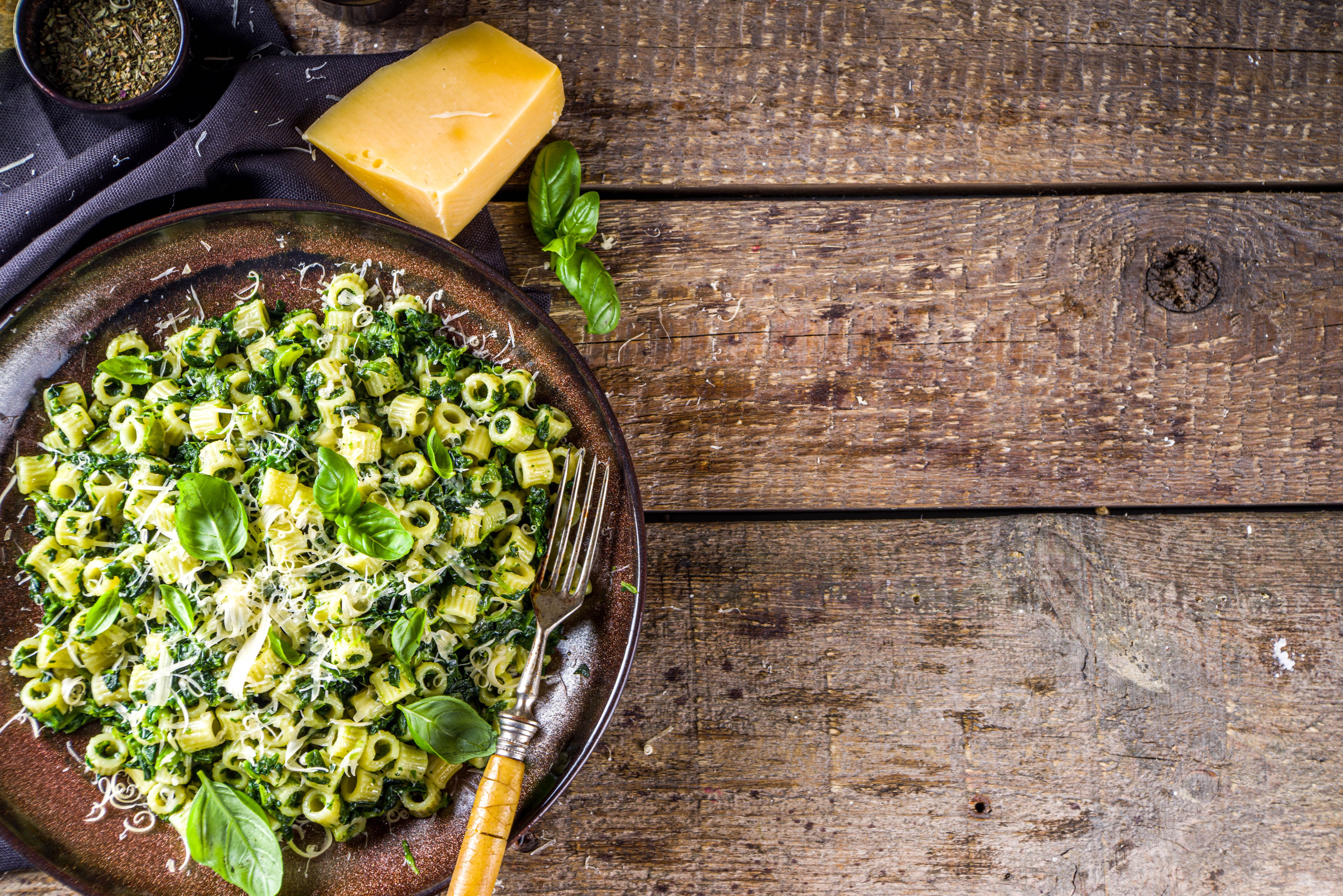 Grüne Ditalini-Nudeln mit Spinat, Pesto und geriebenem Käse auf einem Teller, daneben Parmesan.