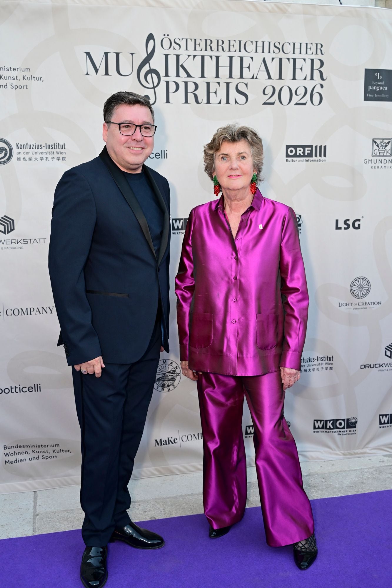 Ein Mann im Anzug und eine Frau im lila Hosenanzug posieren beim Musiktheaterpreis 2026.