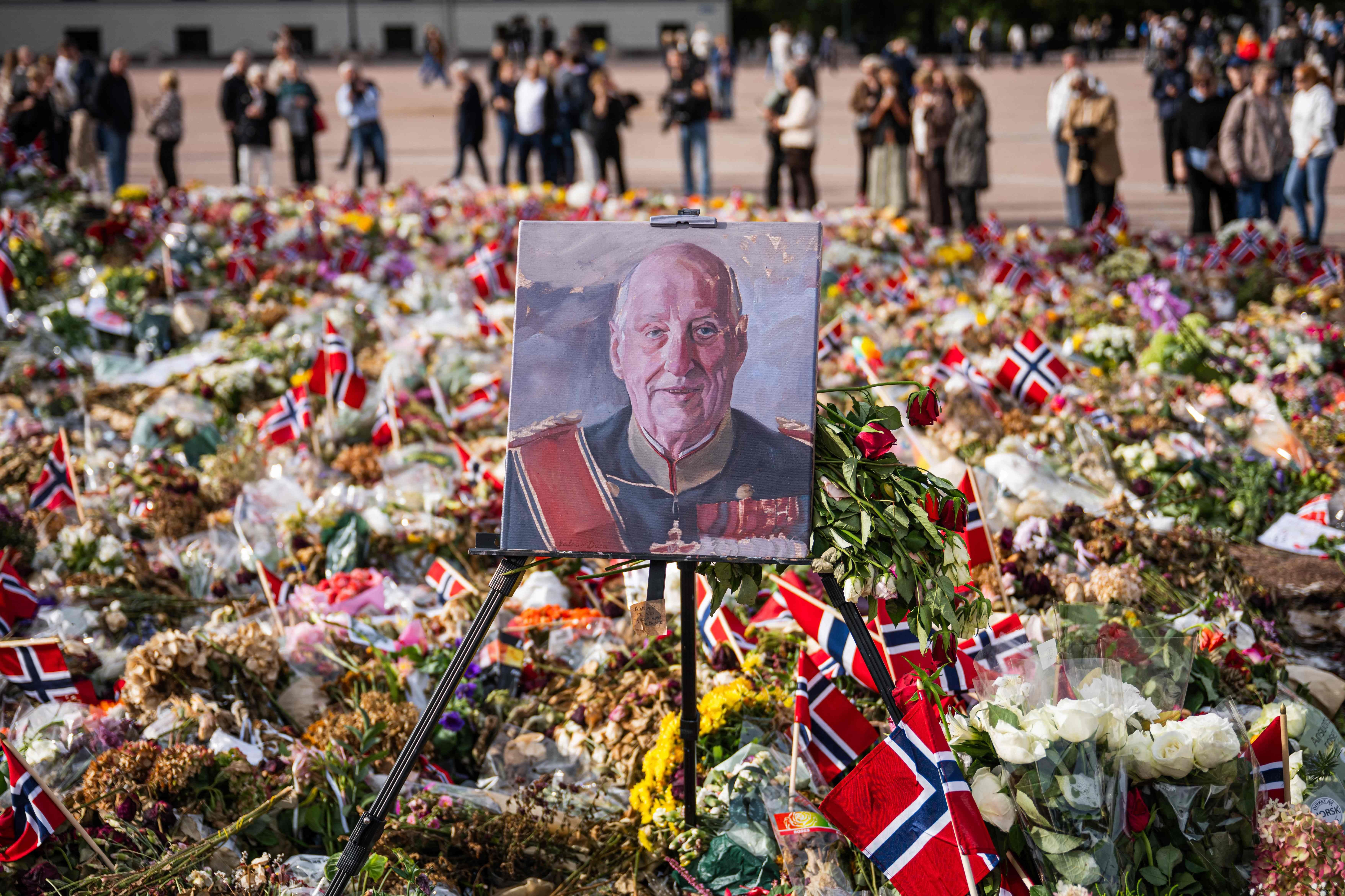Ein Gemälde von König Harald V. steht zwischen Blumen und norwegischen Flaggen bei einer Gedenkstätte.