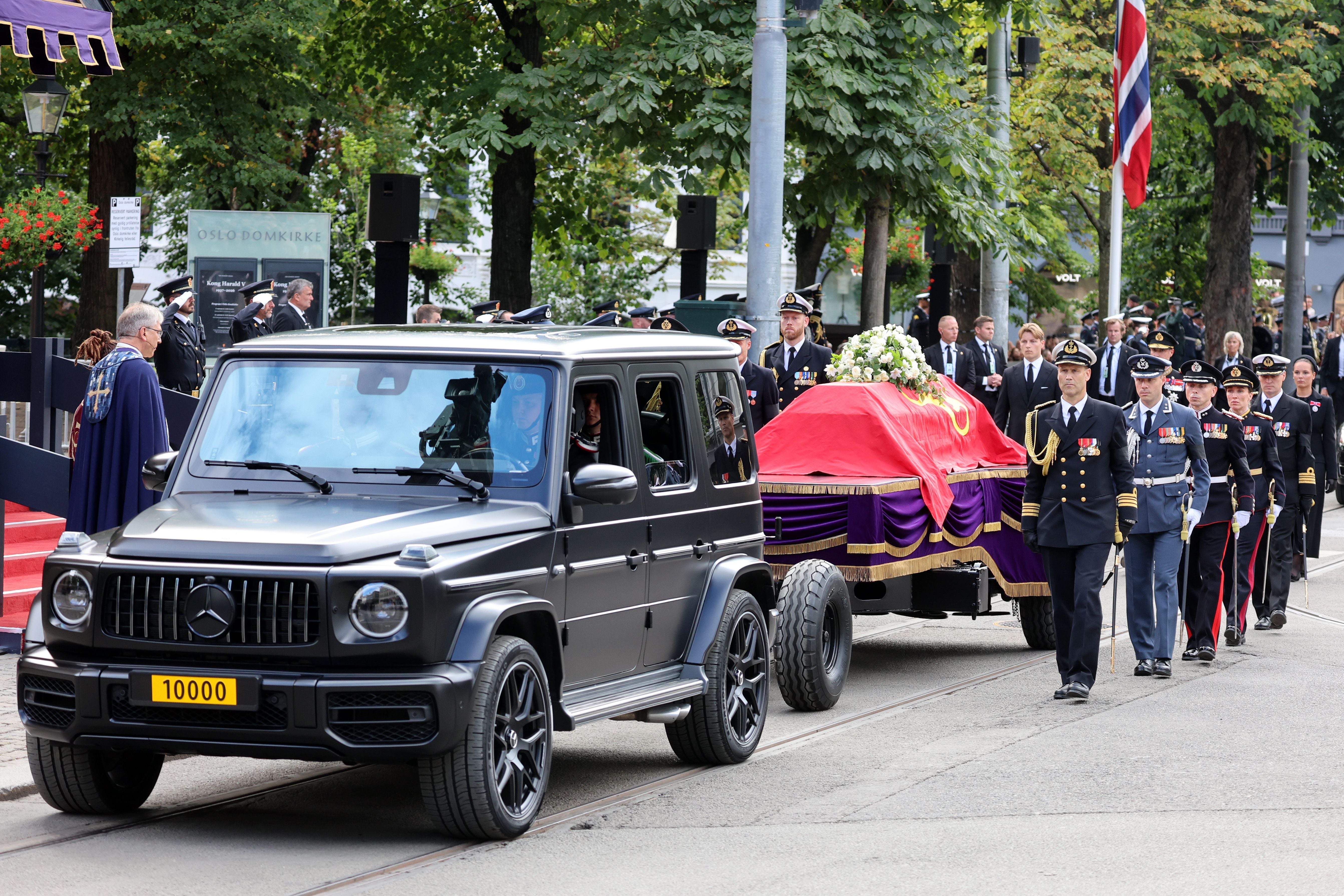 Ein Trauerzug mit einem von Soldaten begleiteten Sarg wird von einem schwarzen Geländewagen gezogen.