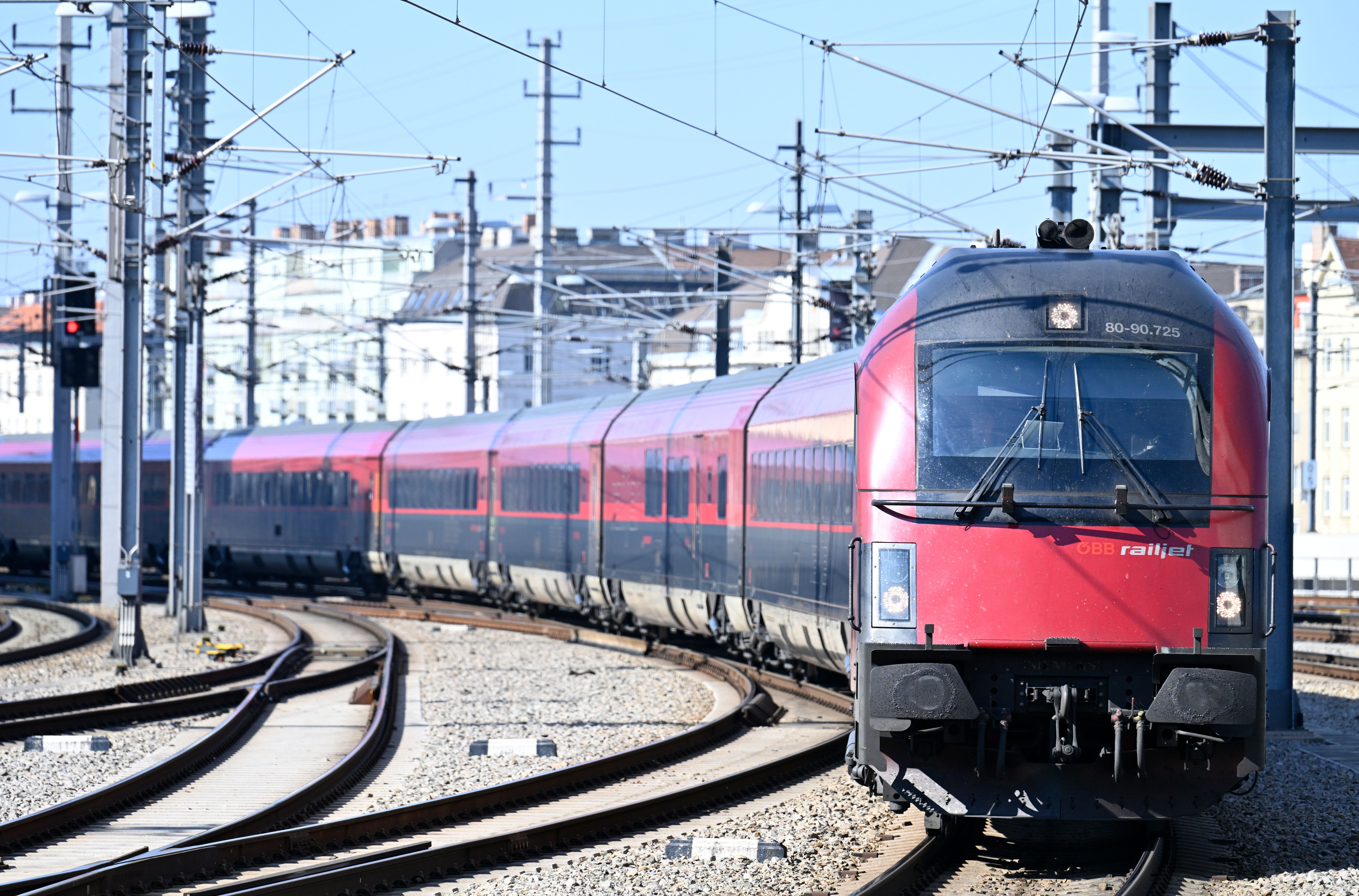 Ein roter Railjet-Zug der ÖBB fährt am Hauptbahnhof in Wien bei Tageslicht entlang der Gleise.