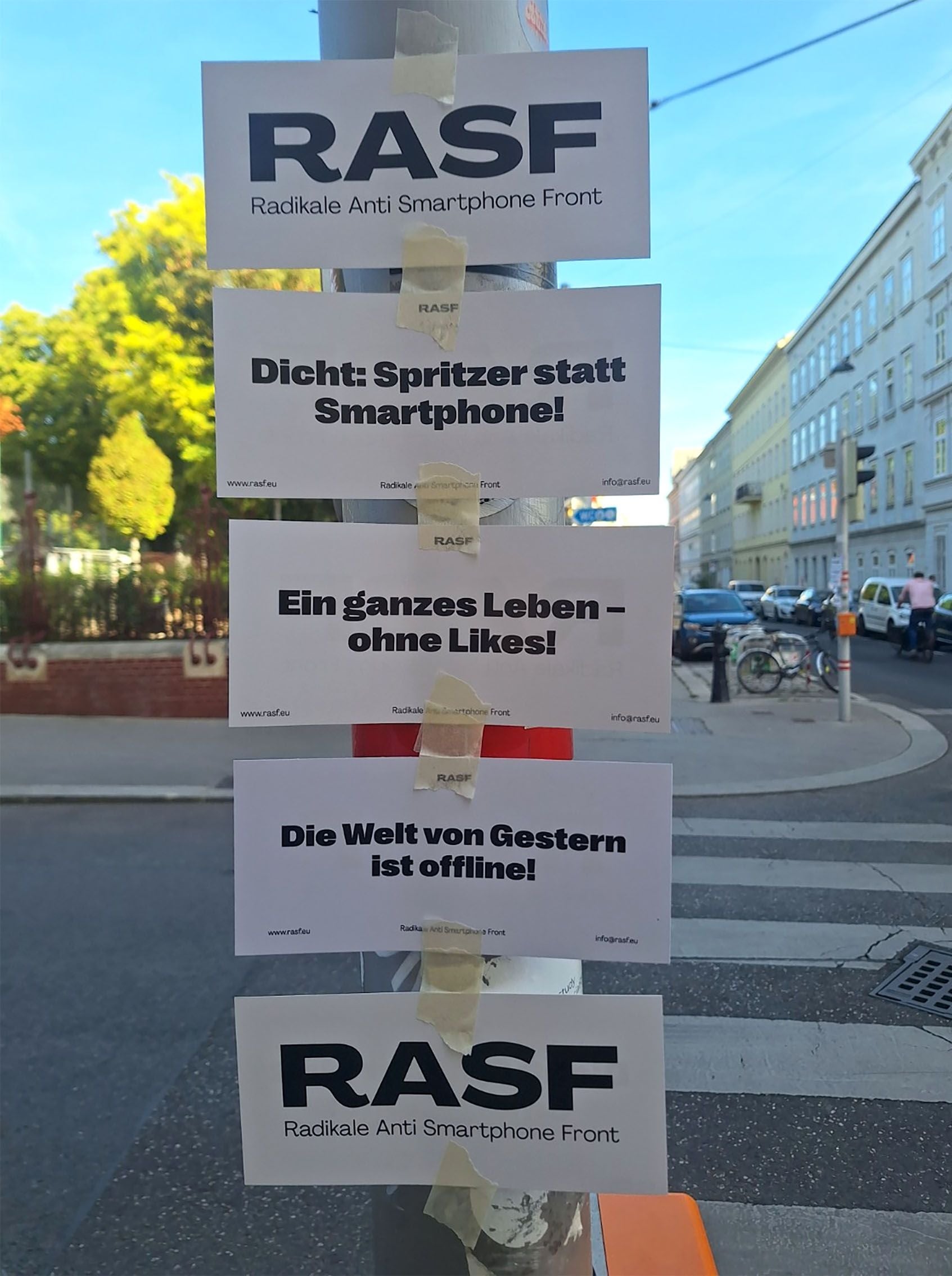 Mehrere RASF-Plakate mit kritischen Sprüchen zu Smartphones kleben an einem Straßenmast in Wien.