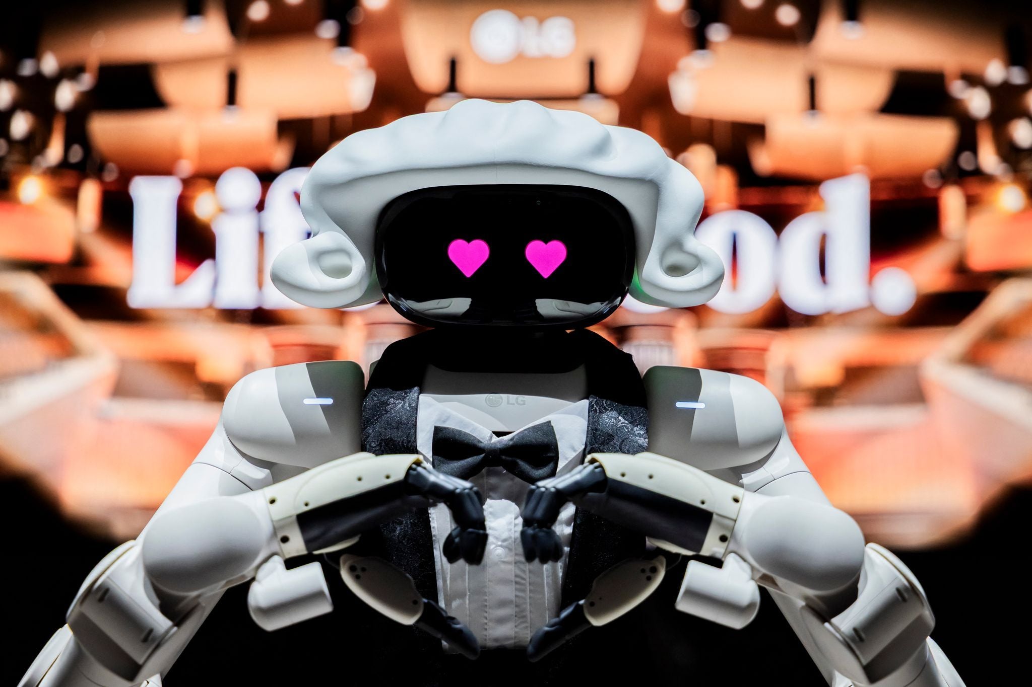 Ein als Dirigent verkleideter Roboter formt ein Herz mit den Händen, Herzaugen auf dem Display.