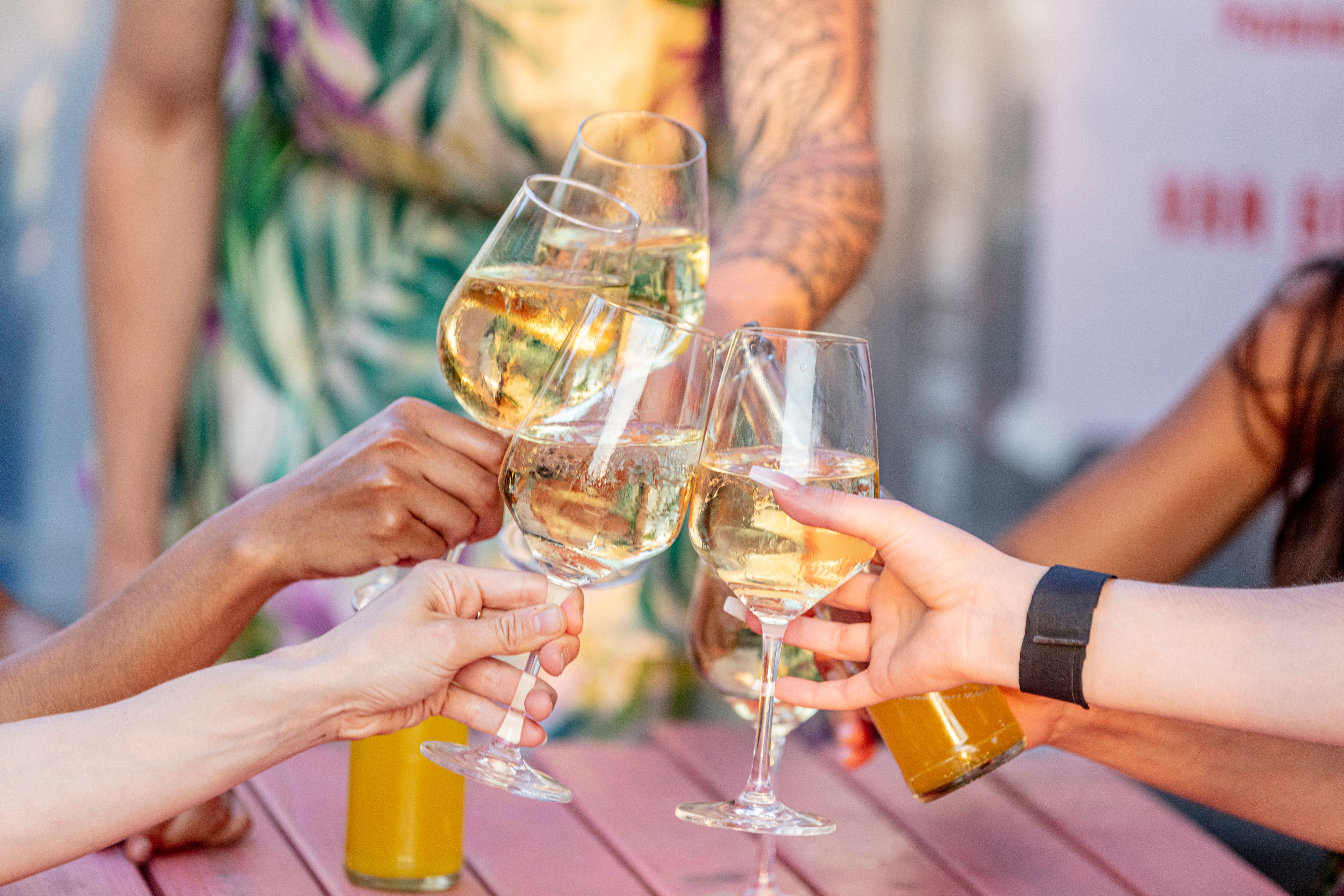 Fünf Personen stoßen mit Gläsern Weißwein über einem Holztisch an.
