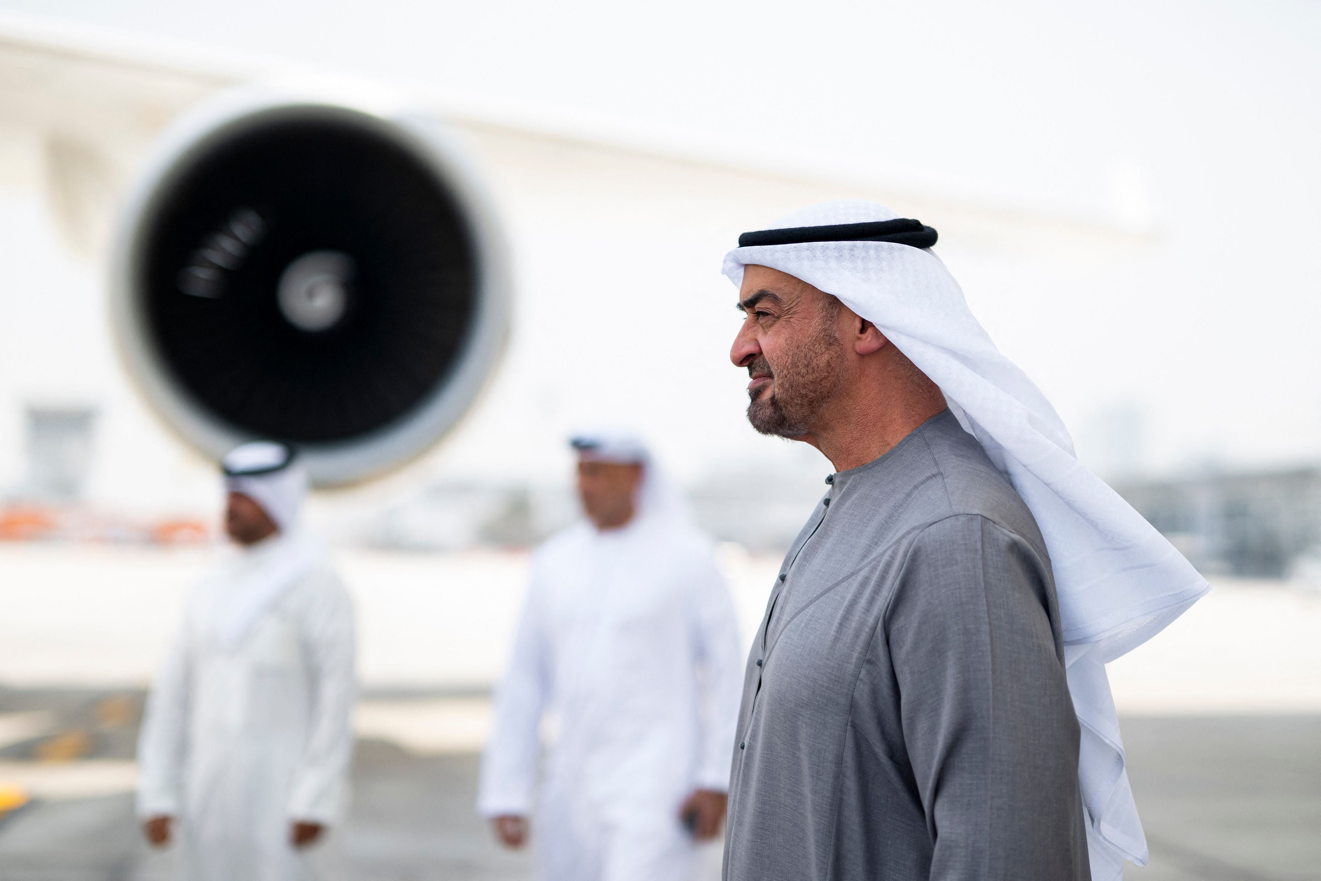 Ein Mann in traditioneller Kleidung steht am Flughafen vor einem Flugzeugtriebwerk.