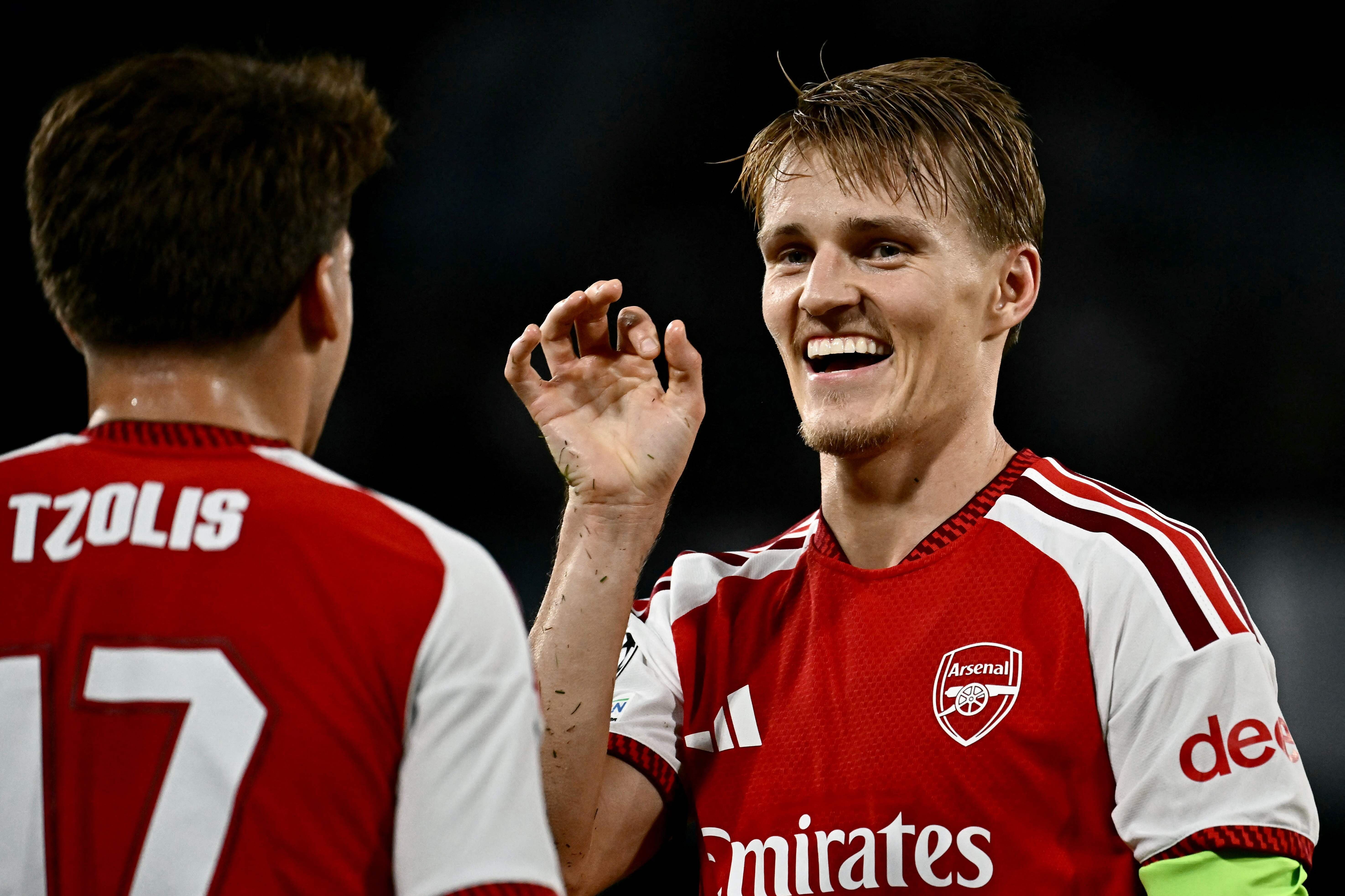 Martin Ödegaard und Christos Tzolis im Trikot des FC Arsenal lächeln und jubeln auf dem Spielfeld.