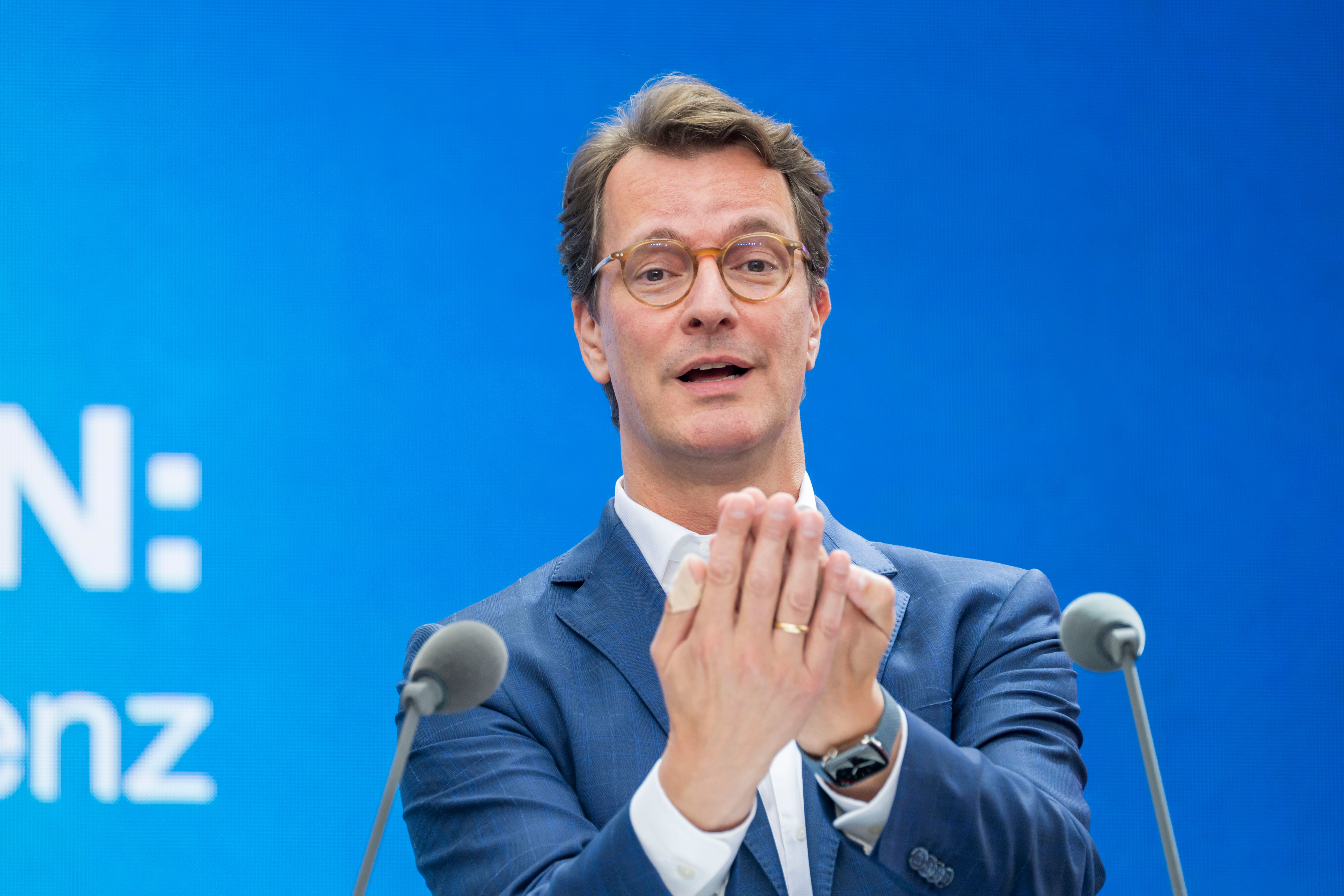 Ein Mann im blauen Anzug spricht auf einer Bühne vor blauem Hintergrund zwischen zwei Mikrofonen.