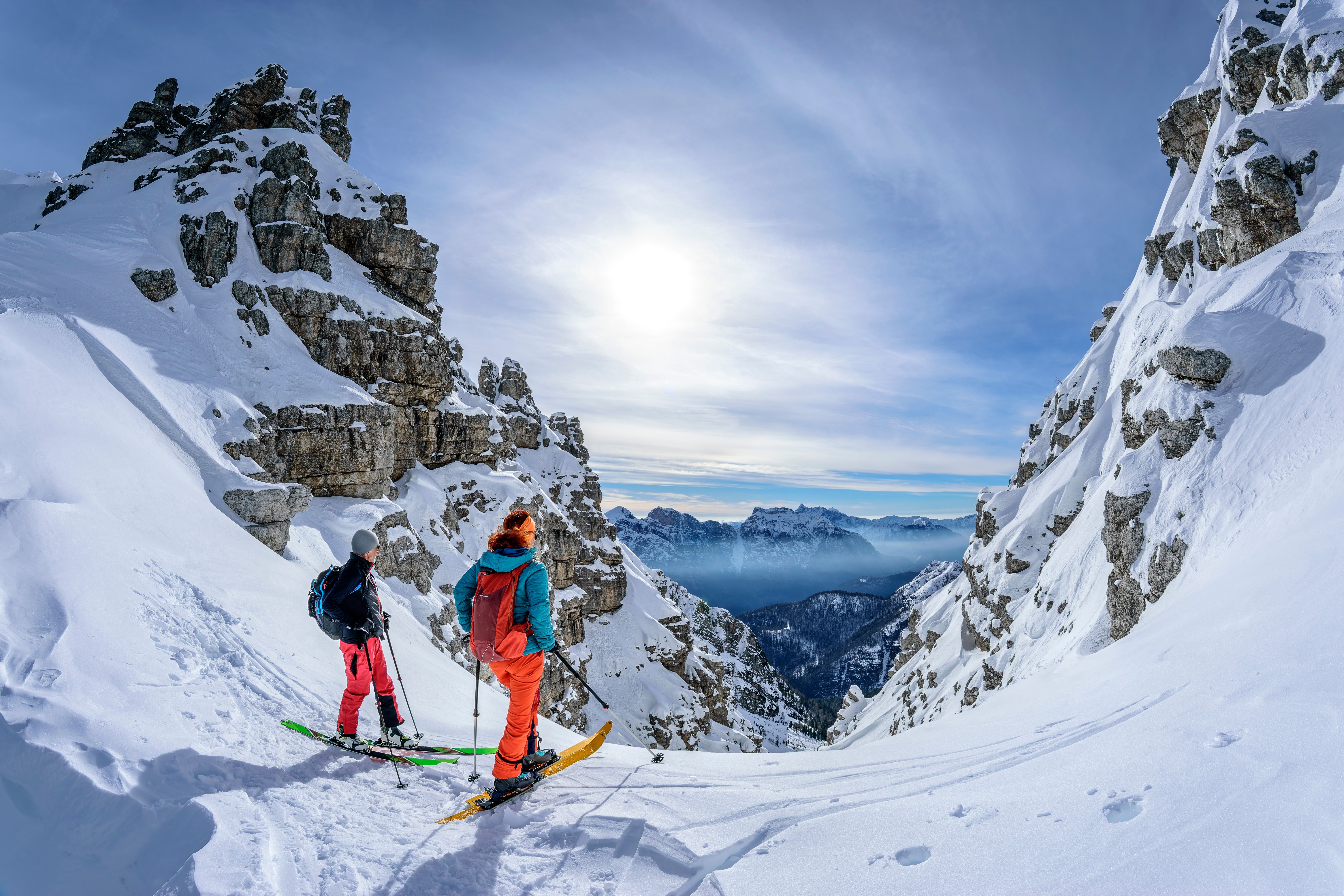 Zwei Skitourengeher stehen in verschneiten Bergen und blicken ins sonnige Tal hinab.