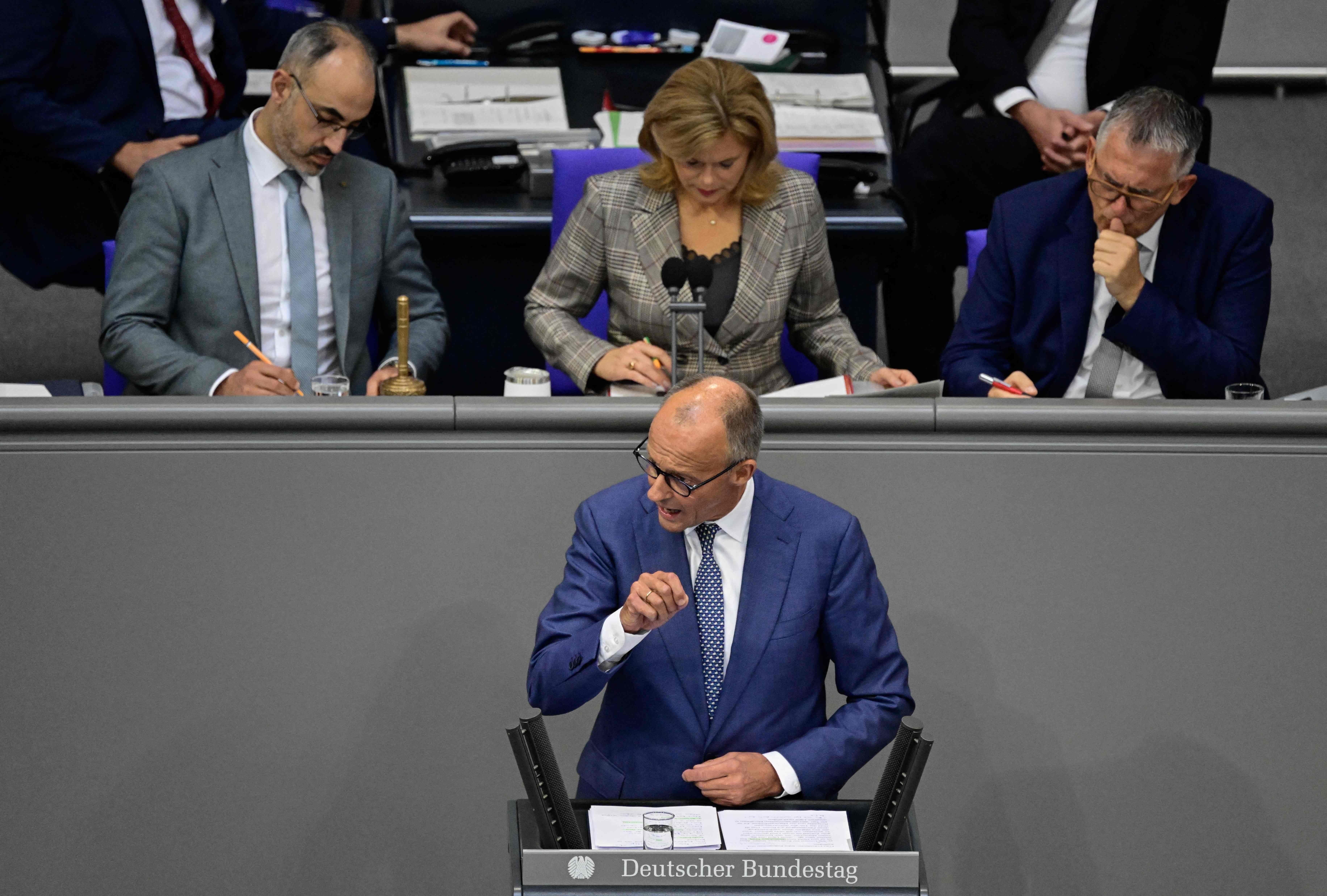 Ein Mann hält im Plenarsaal des Deutschen Bundestags eine Rede, drei Personen sitzen dahinter.