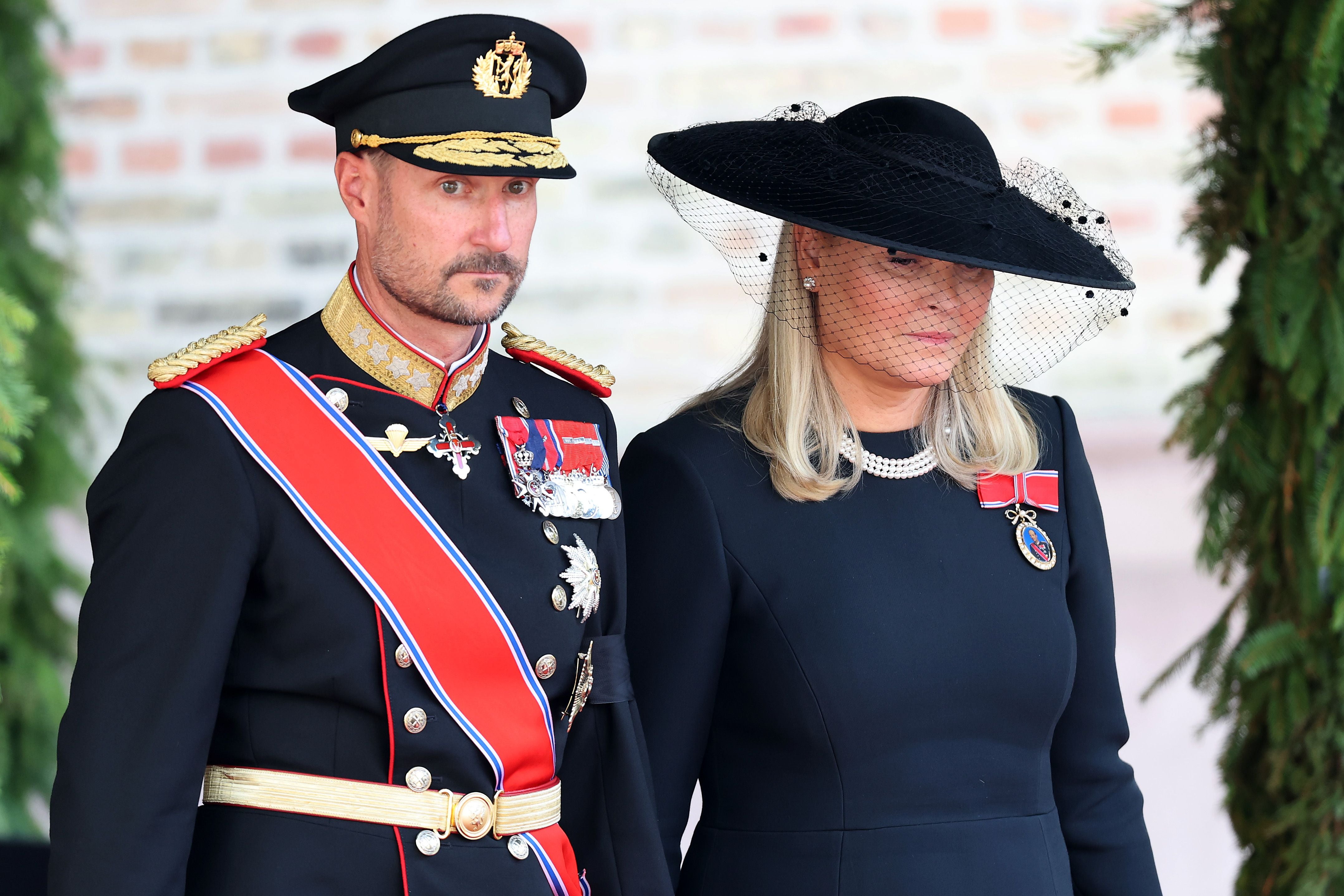Ein Mann in Militäruniform und eine Frau in schwarzem Kleid und Hut stehen nebeneinander.
