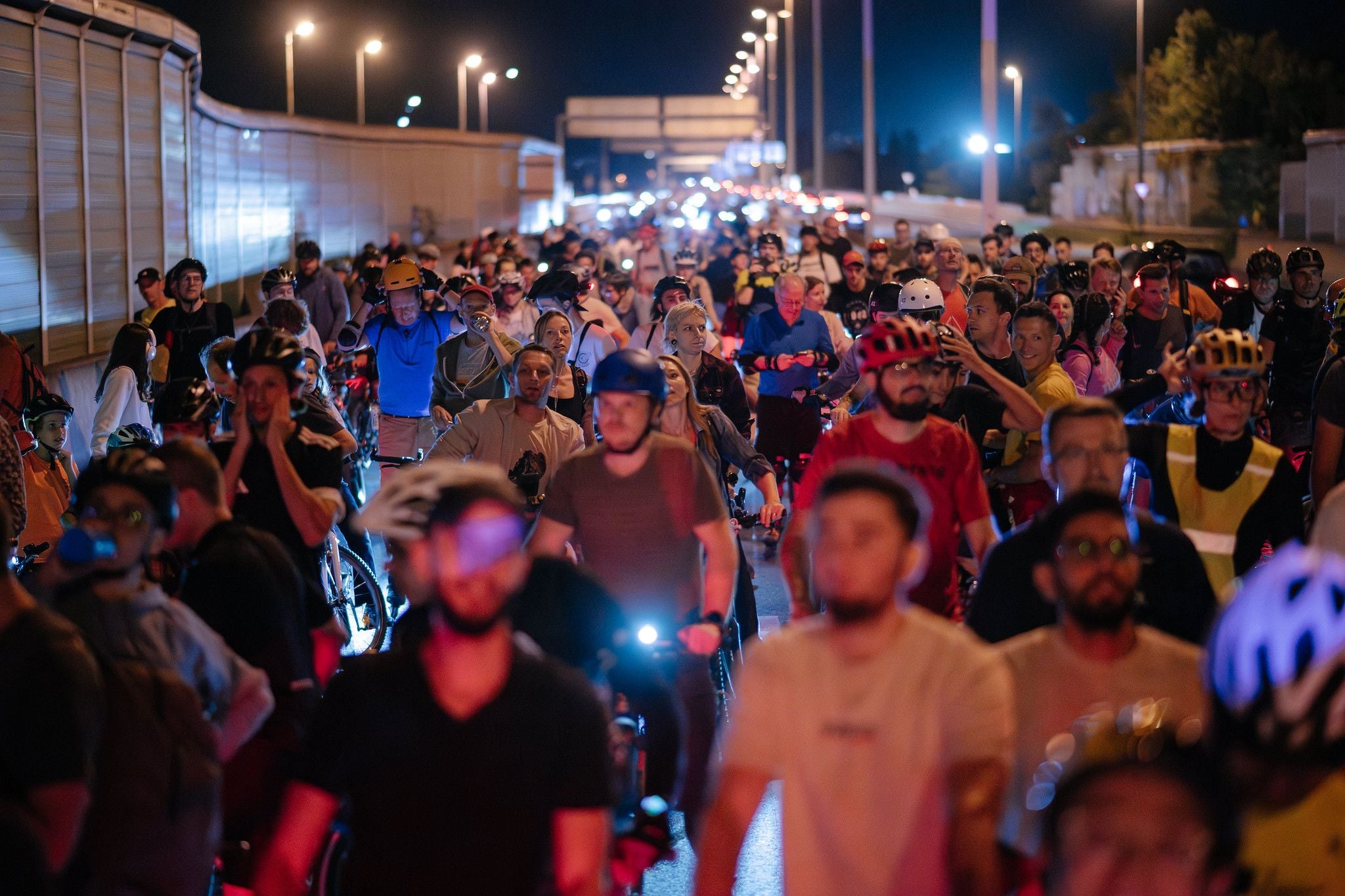 Große Gruppe von Menschen mit Helmen skatet nachts auf einer beleuchteten Straße.