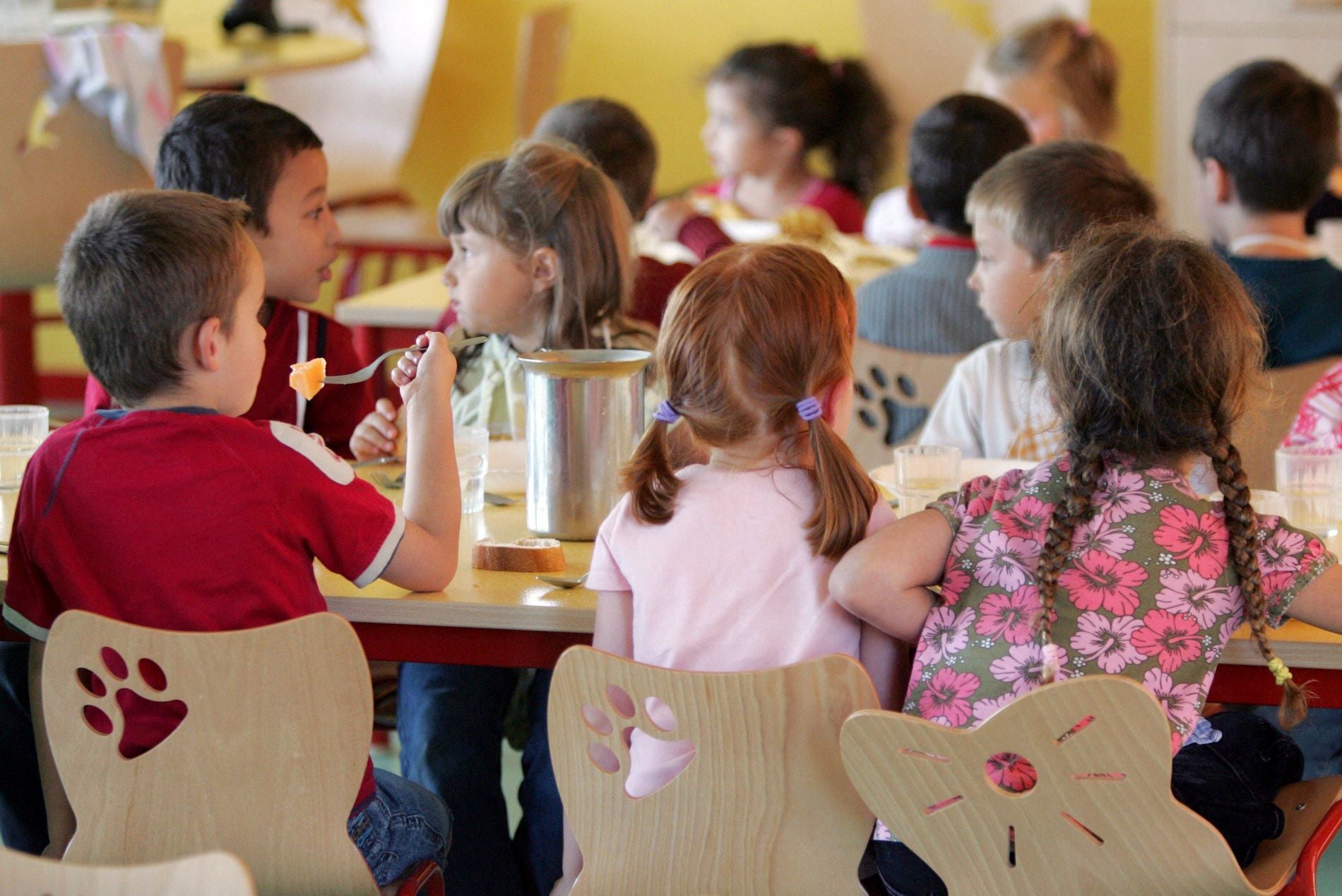Kinder sitzen in einer Schulkantine und essen gemeinsam an Tischen.